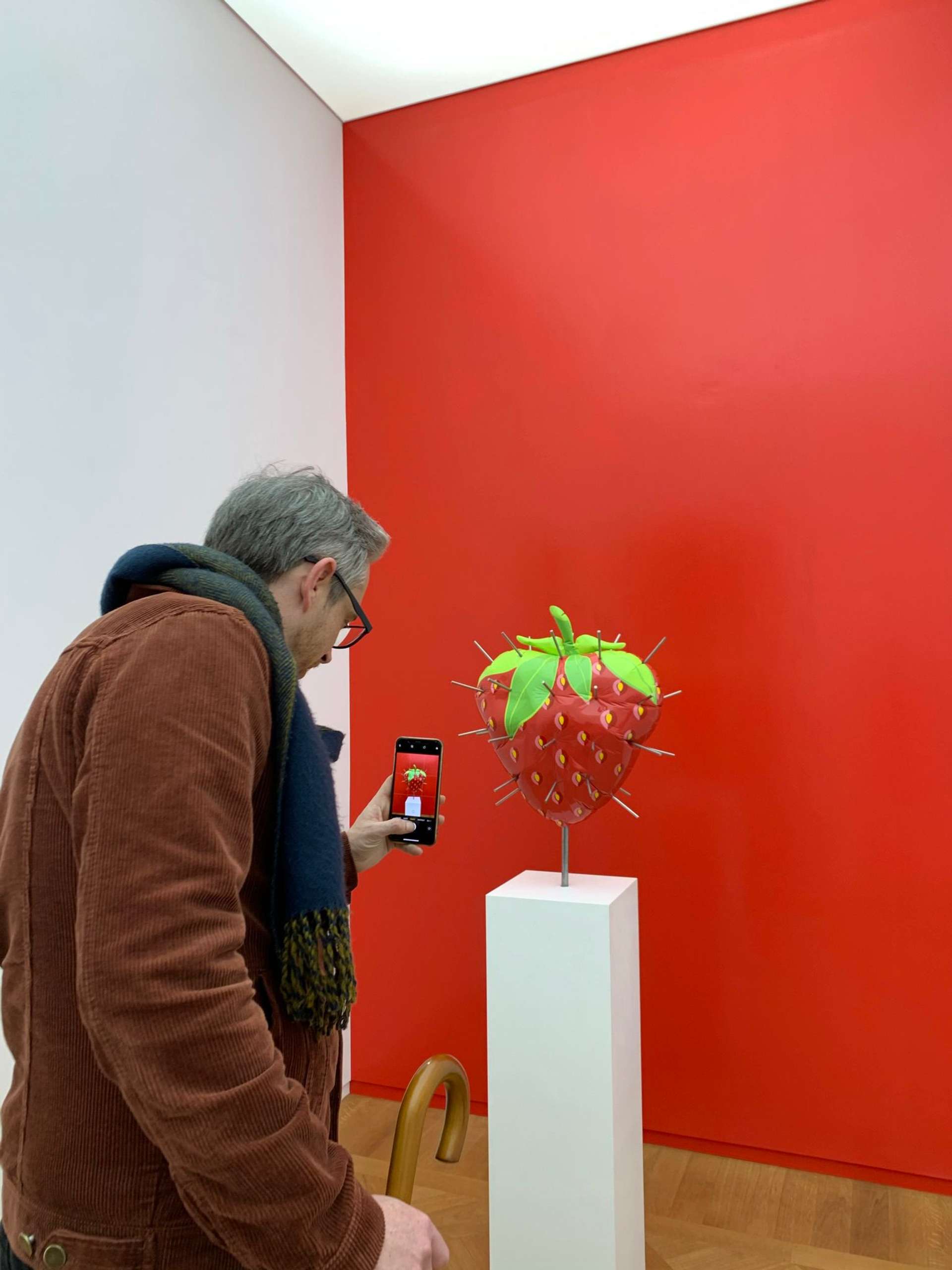 Millennial man taking a photo of a sculpted artwork of a strawberry on his mobile phone.