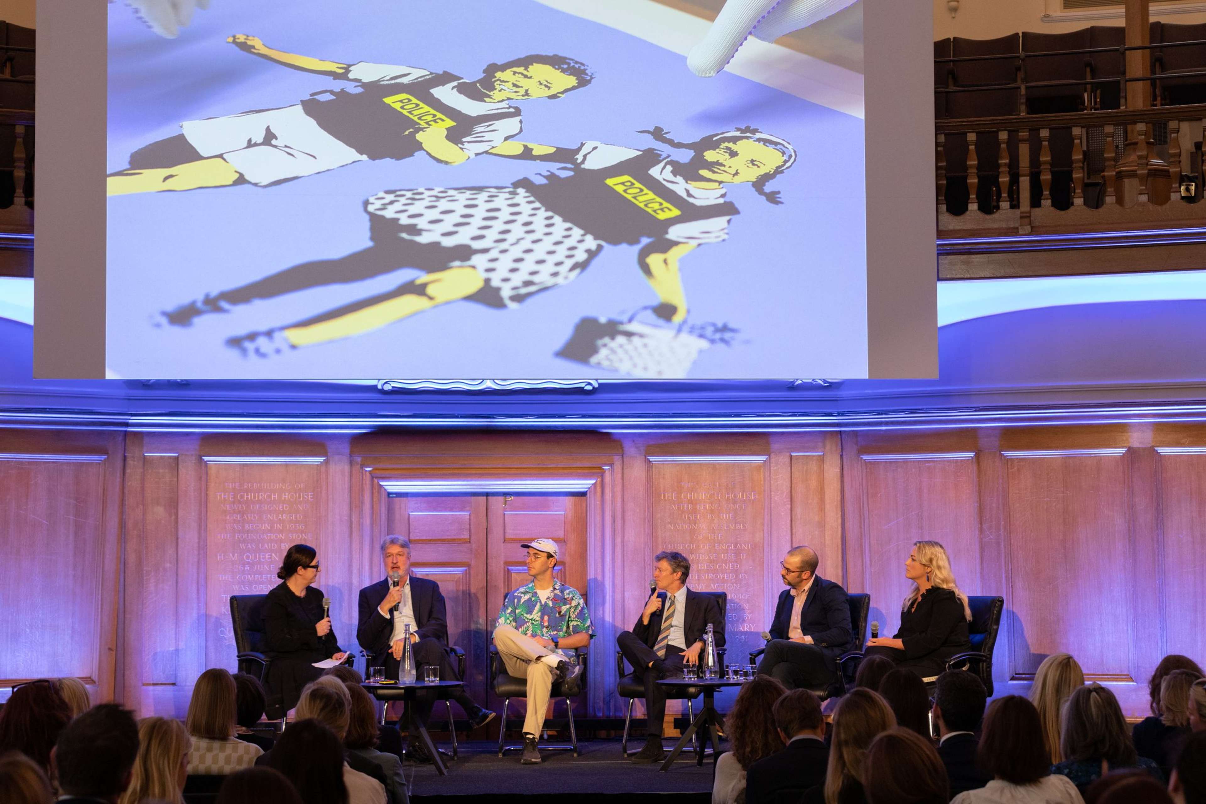 A panel of five guests and one host, under a projected Banksy print