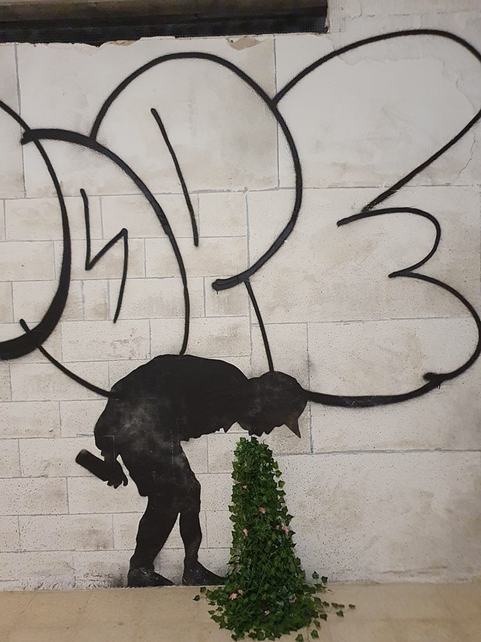 This graffiti shows a male figure bent over, apparently vomiting a bouquet of foliage.