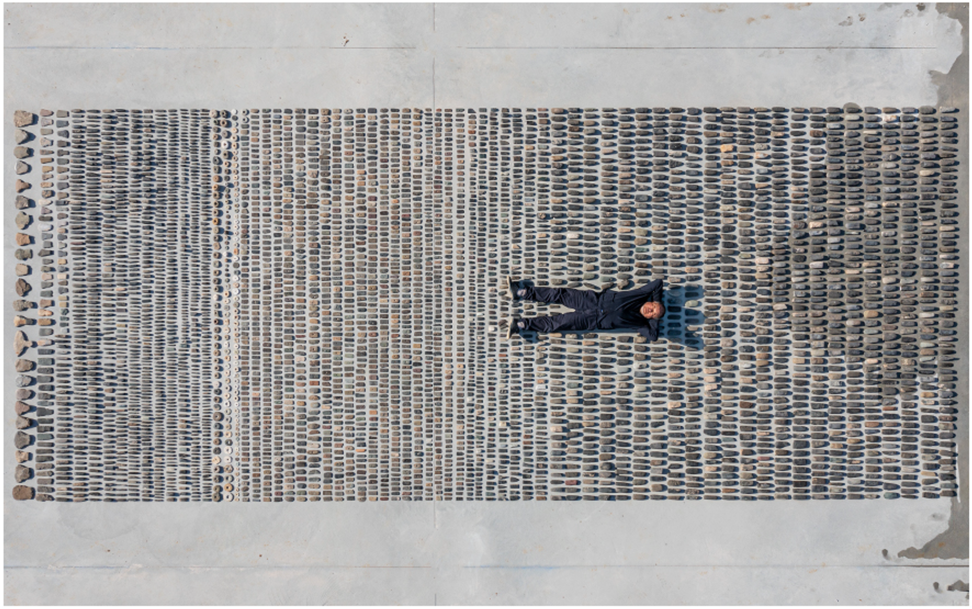 Bird's-eye view photograph of Ai WeiWei lying in the upper center of a vast collection of assembled and disassembled Chinese artifacts. His legs are spread apart, and his arms are positioned behind his head.