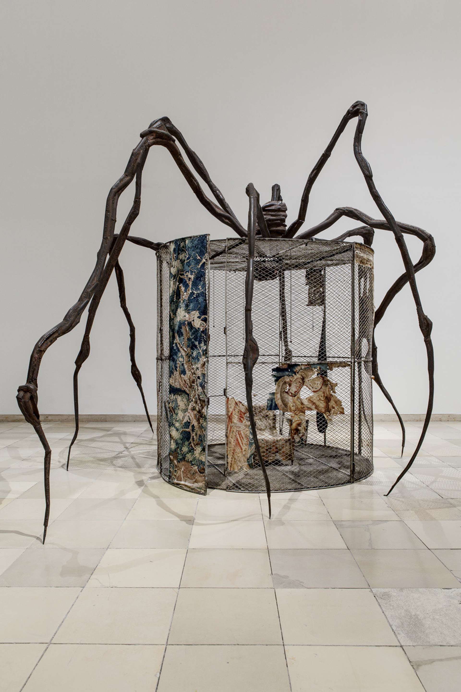 A spider sculpture by Louise Bourgeois engulfing a cage installation in a gallery.