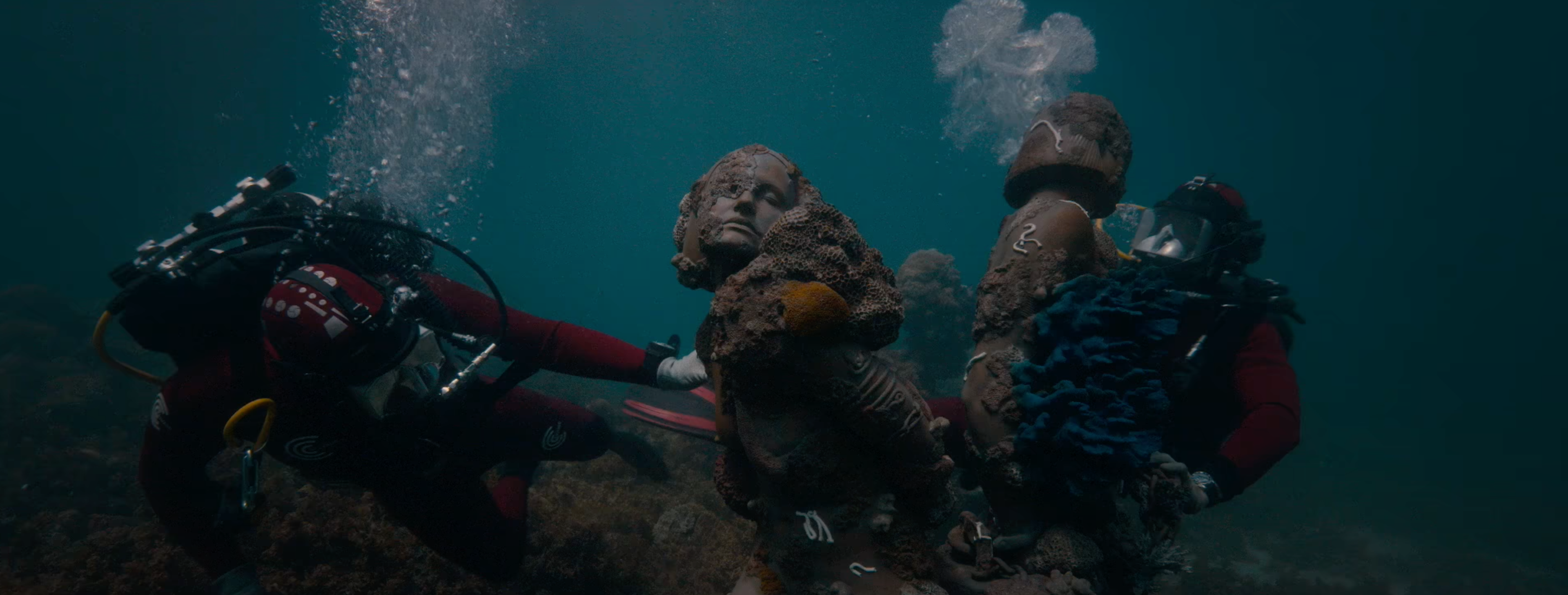This image shows two divers underwater, handling two statues.