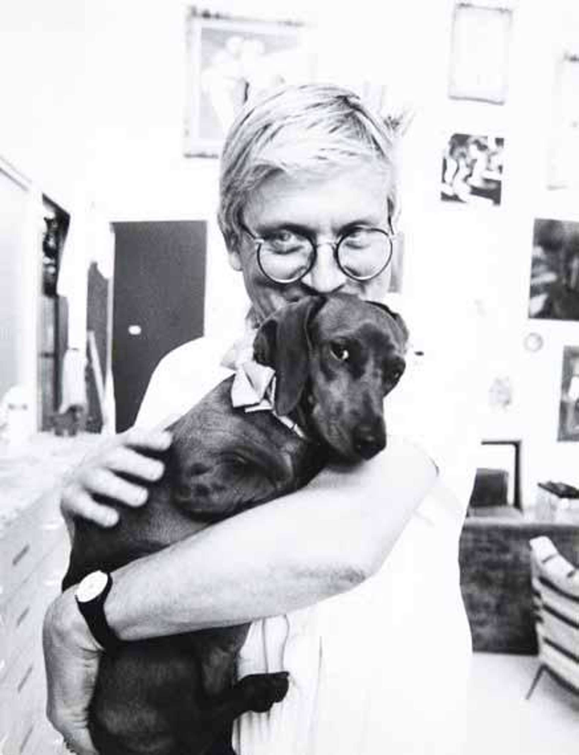 A monochrome photograph of David Hockney cuddling one of his beloved Dachshunds.