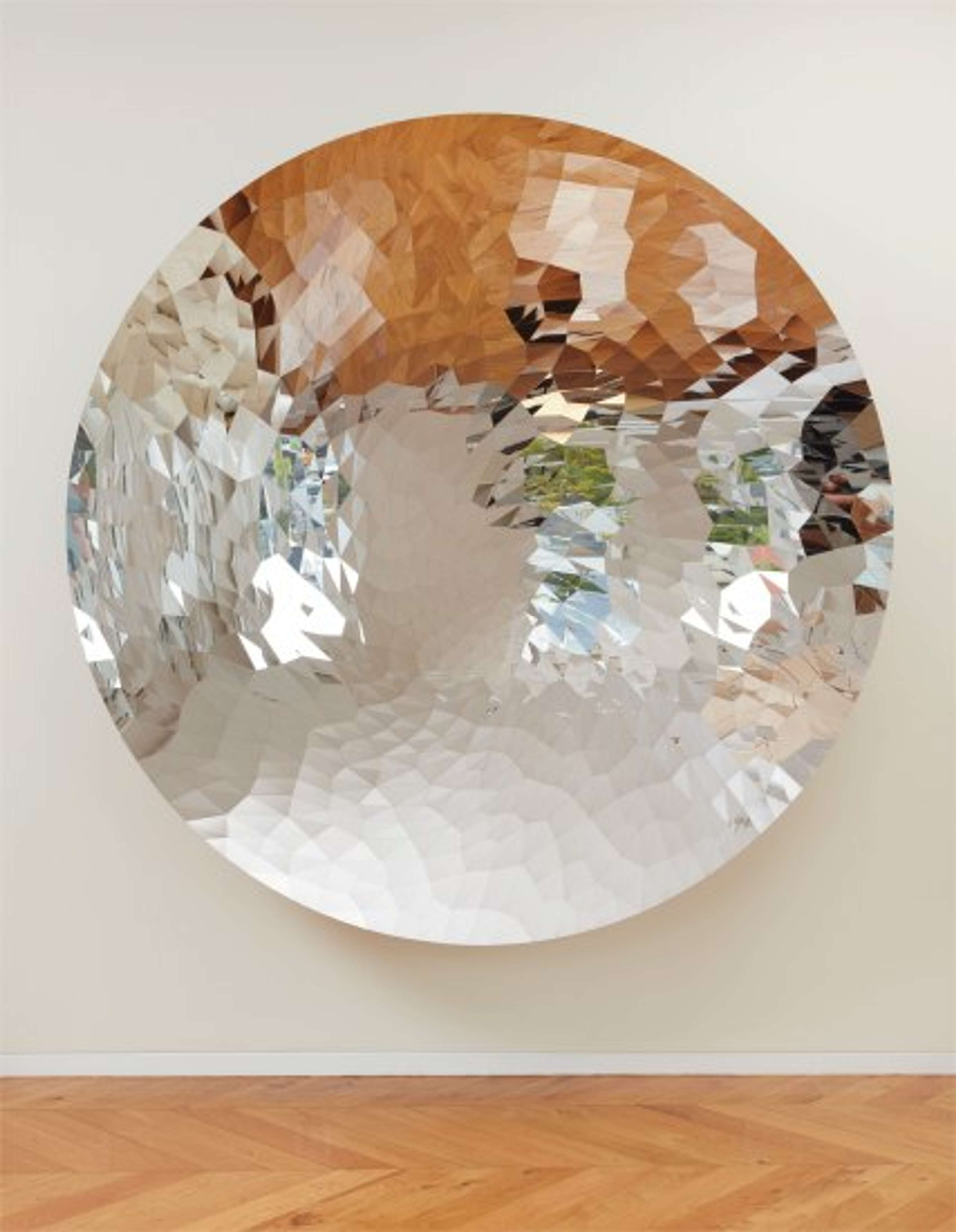 A circular stainless steel mirror disc with a surface that is fragmented into countless irregular shapes, each facing a slightly different angle to those around it. The result is to break up the inverted reflection of the gallery space around it into irregular shapes of colour.