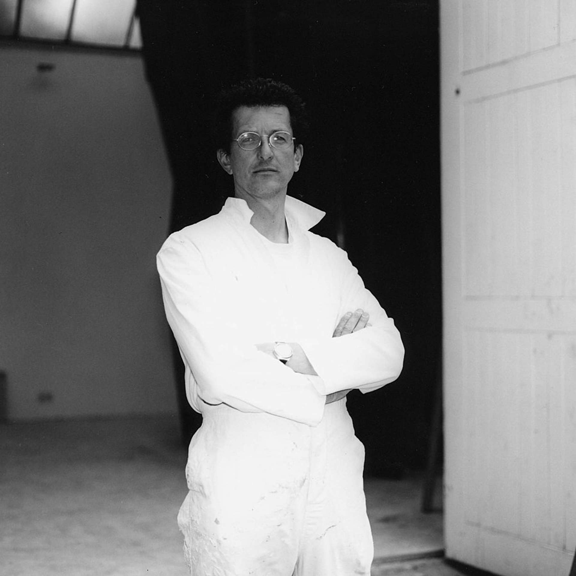 A black and white photographic portrait of artist Antony Gormley, from the waist up.