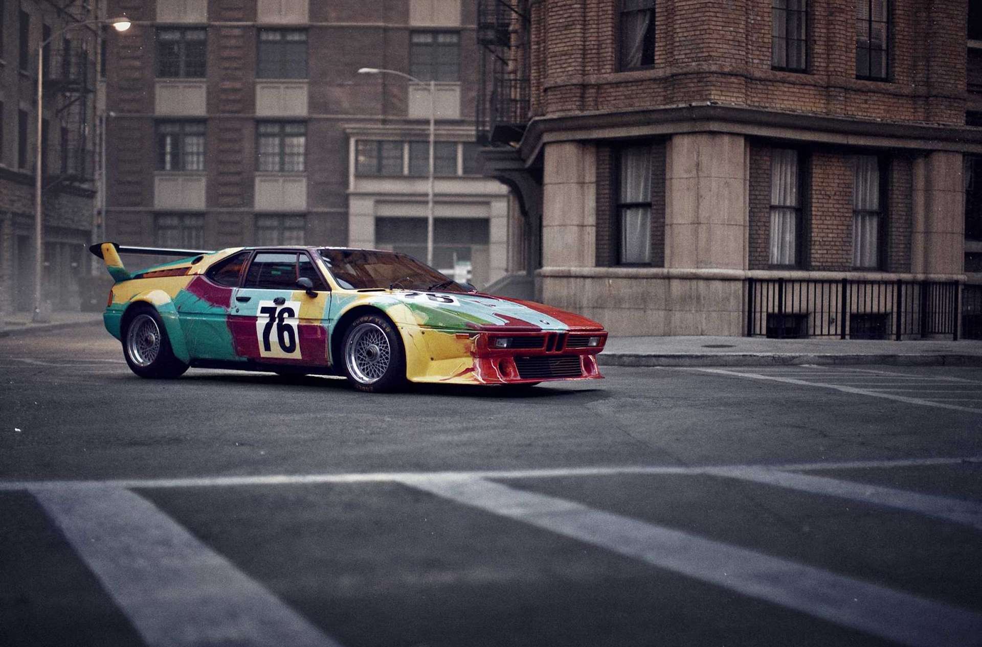  A BMW car designed by Andy Warhol in 1979, covered in vibrant, multi-coloured stripes and brushstrokes reminiscent of Warhol's pop art style.
