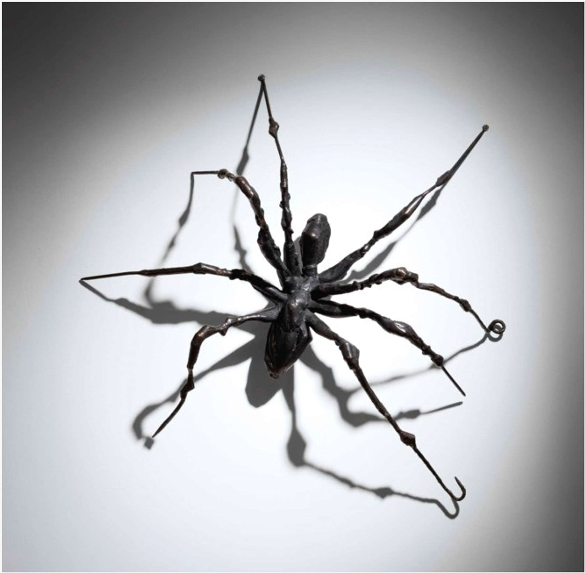 A wall relief spider sculpture climbing upwards with a slight tilt, showcasing a dynamic movement. Its eight legs are evenly balanced on the surface.