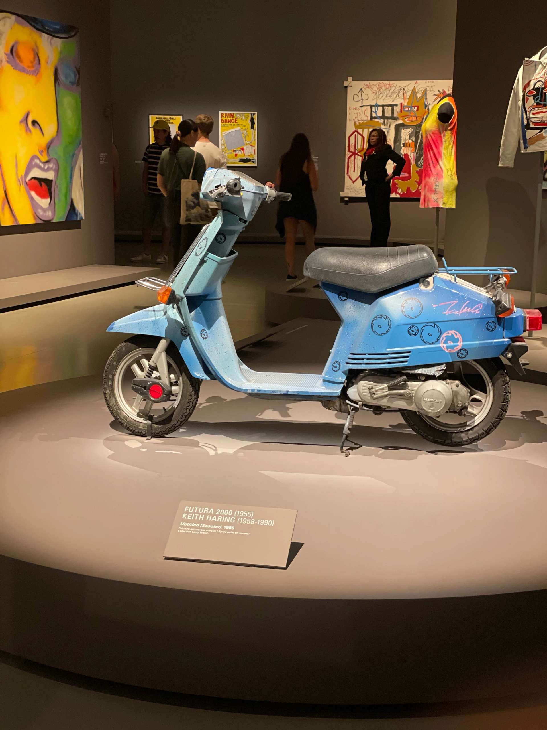 A blue motor scooter in the middle of an art exhibition