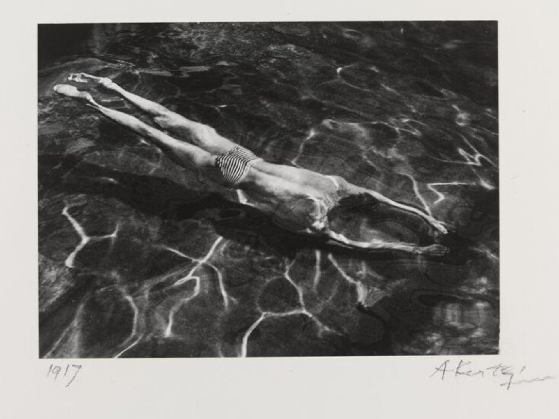 This black and white photograph shows a man swimming underwater.
