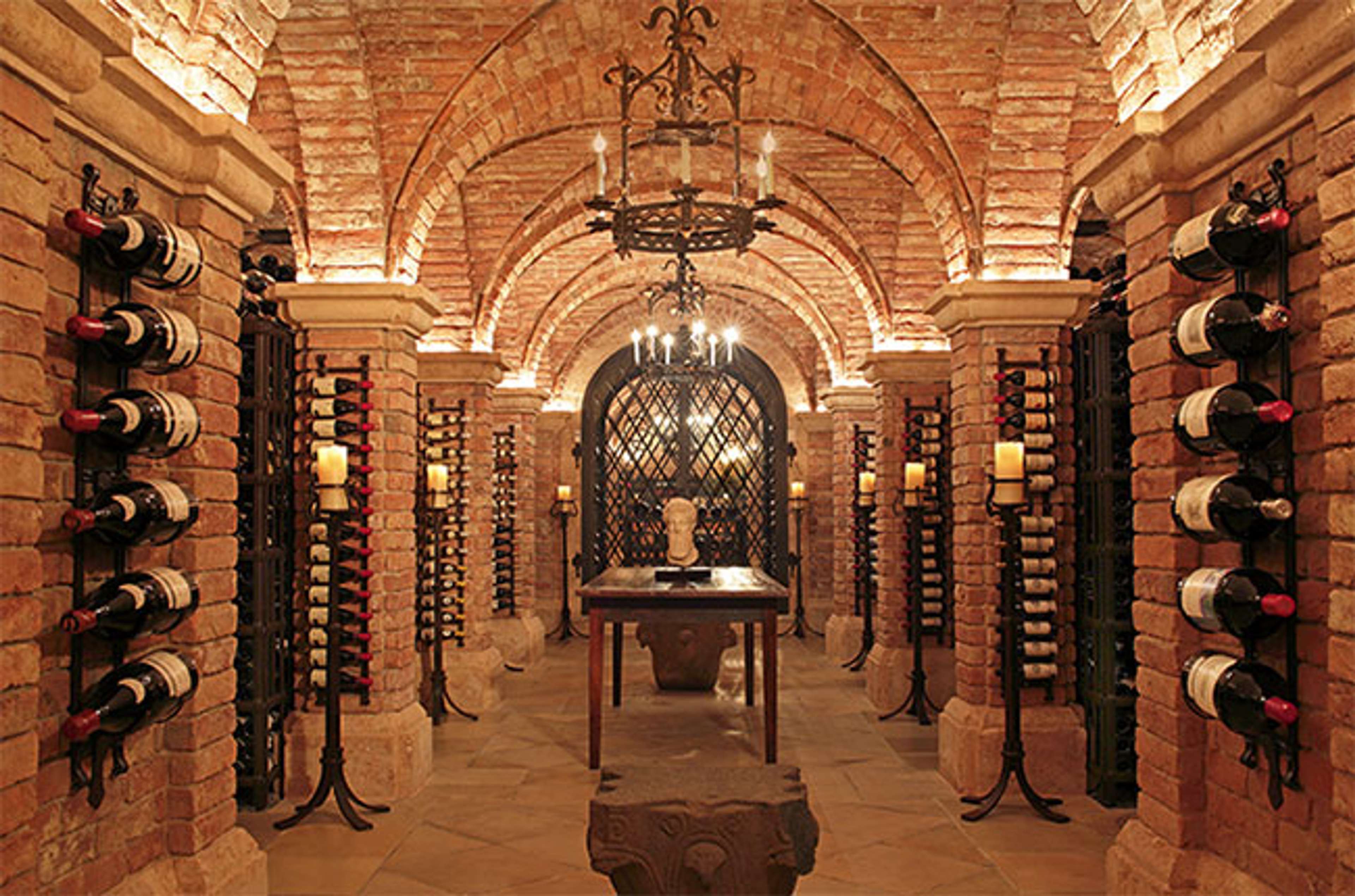 Brick wine cellar with bottles down the side of the walls and a hanging chandelier