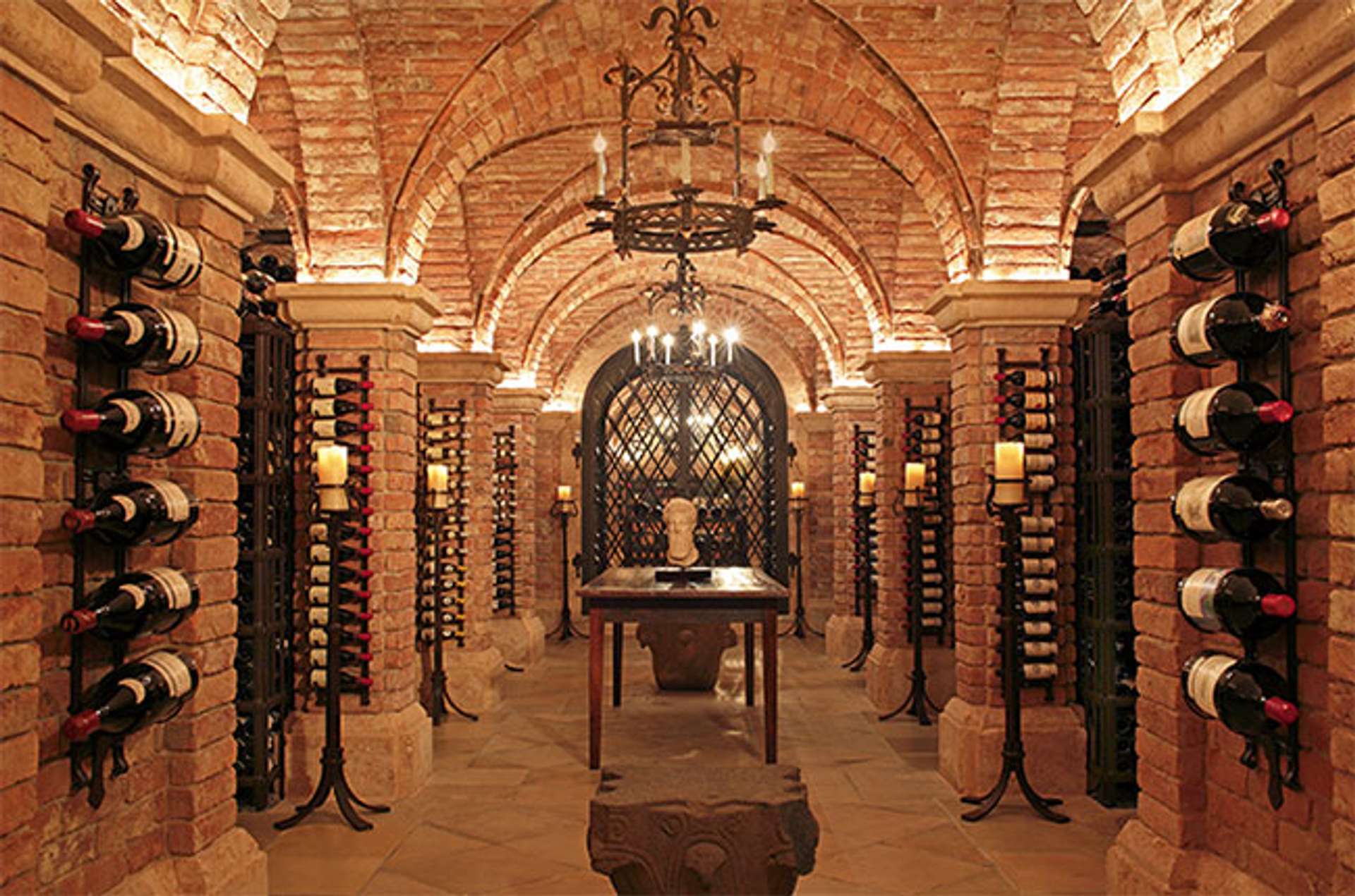 Brick wine cellar with bottles down the side of the walls and a hanging chandelier