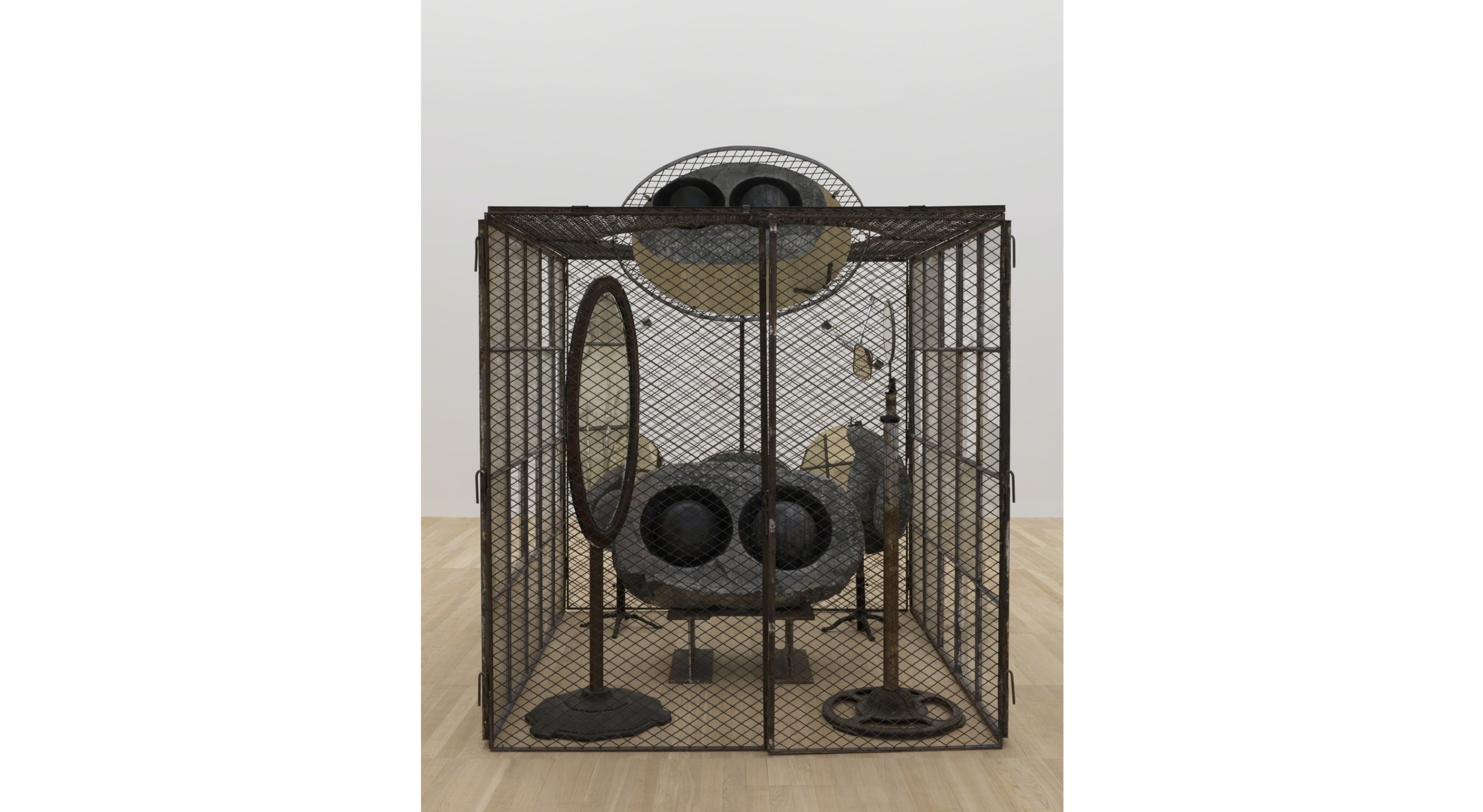 Sculpture of a mesh metal cage with a face inside constructed using a lump of grey stone and two black heavy marbles as eyeballs