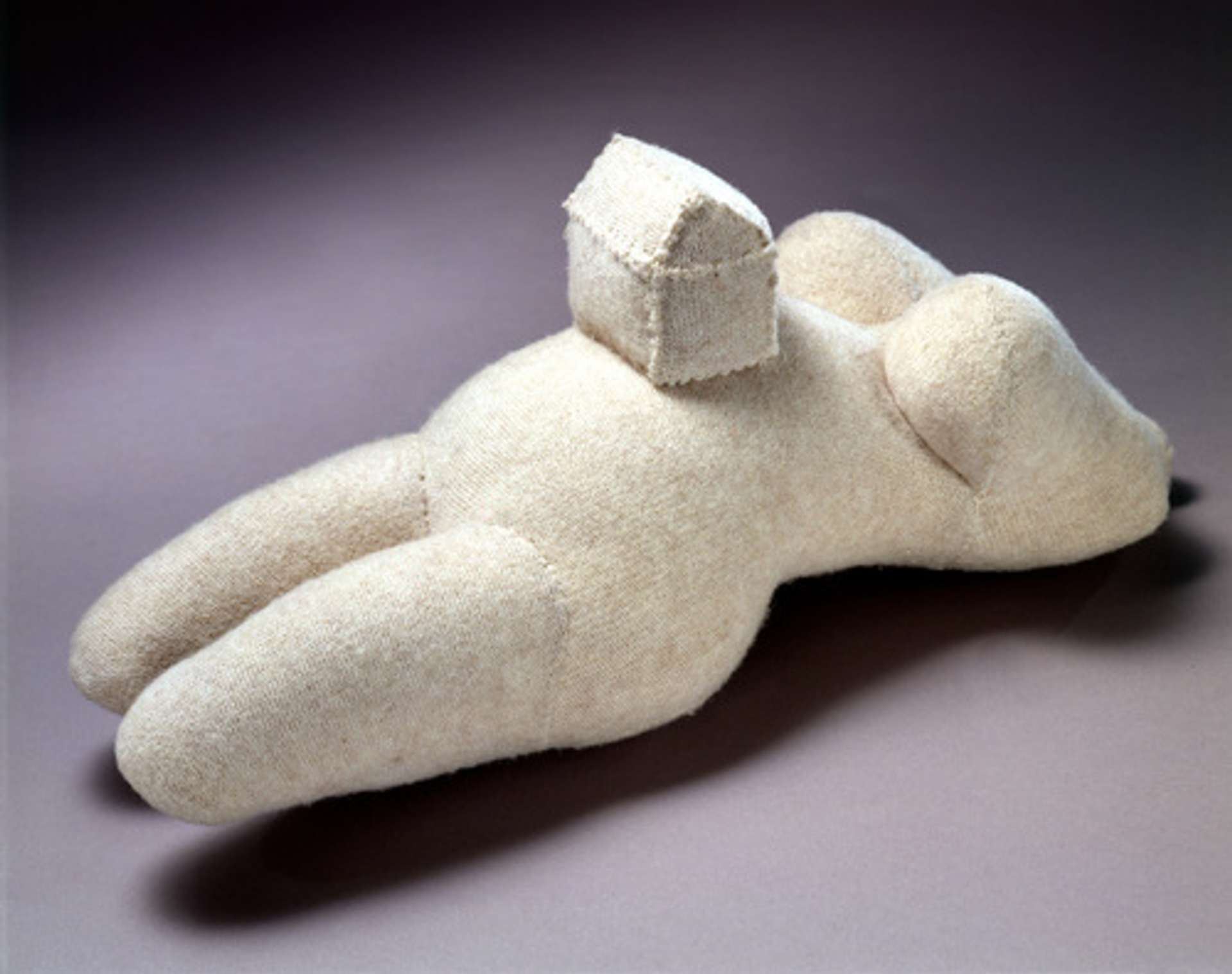 A fabric sculpture of a woman’s body from the cheesy down, with a house sitting on her stomach