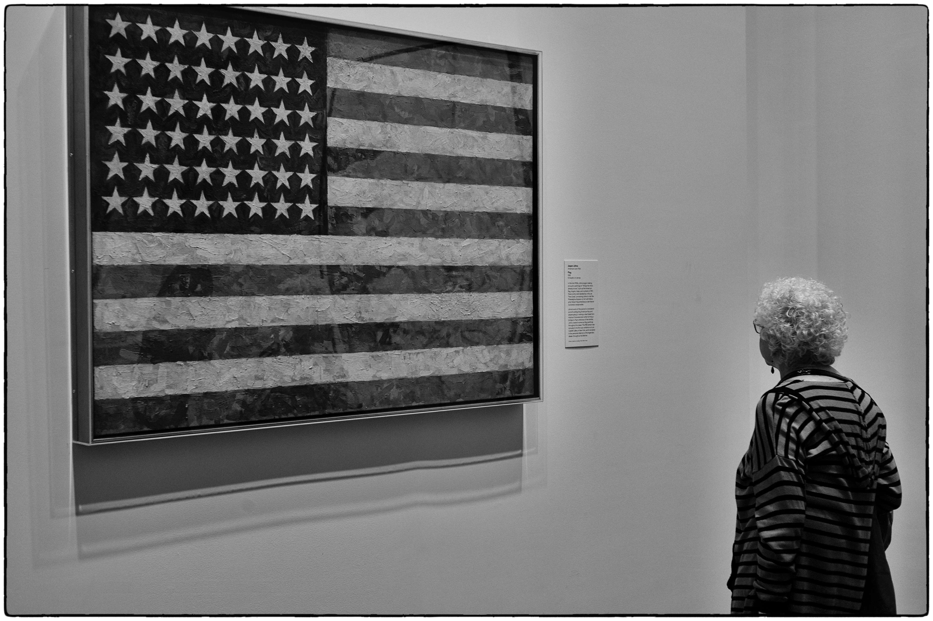 Monochrome photograph of a woman standing in front of a large artwork of an american flag