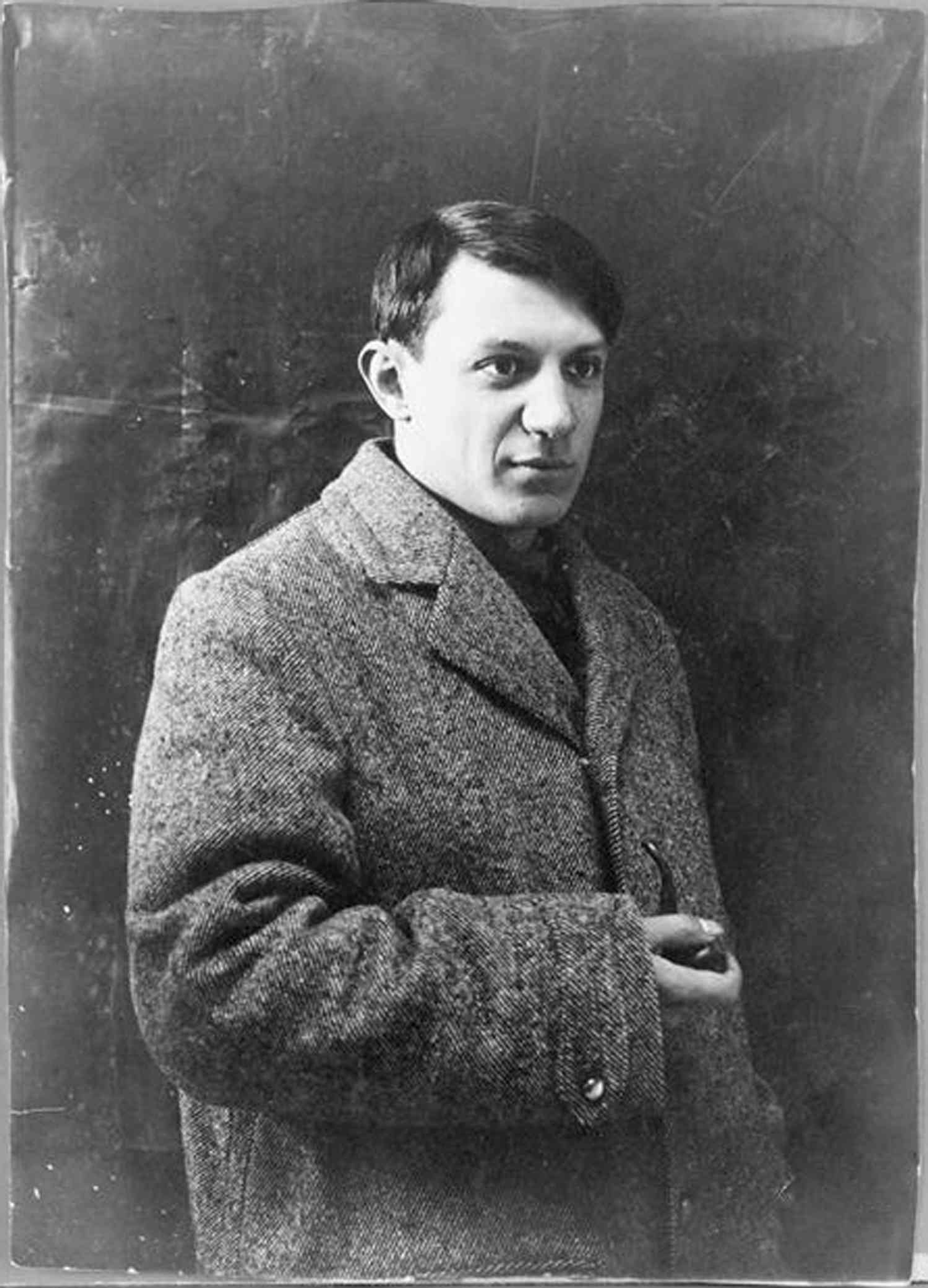 A monochrome photograph of the artist Pablo Picasso as a young man, wearing a woollen coat and looking slightly off camera.
