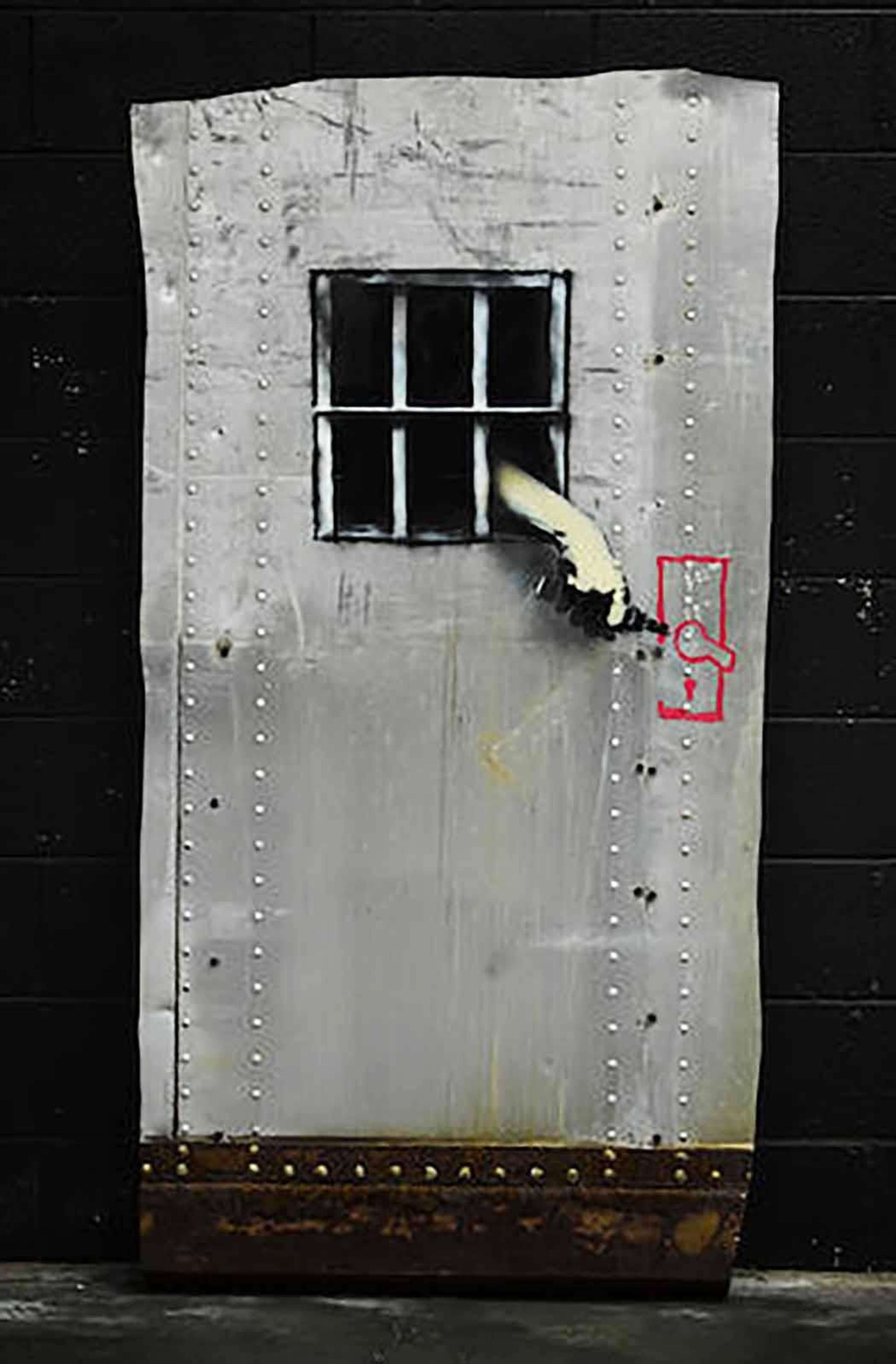 Banksy’s Jail Break. A spray paint work on steel of a hand combing out of bars to unlock a jail door.