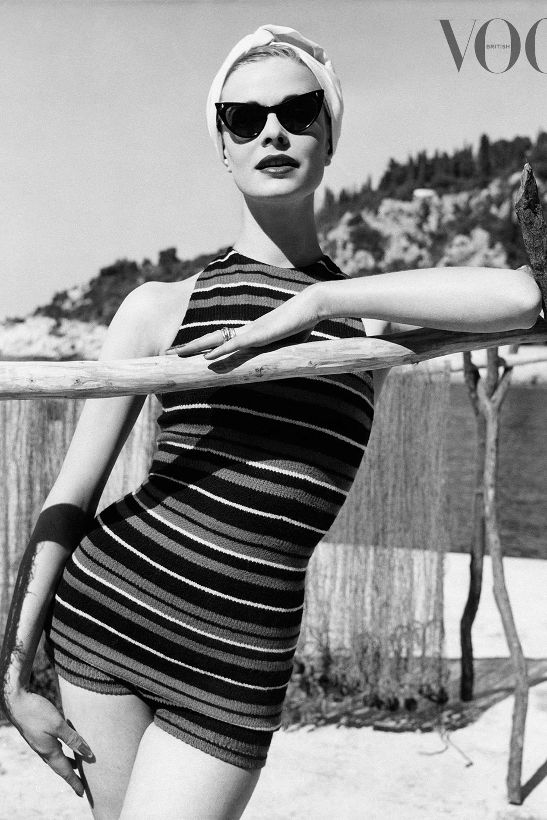 A black and white image of a model wearing a vintage-style pair of sunglasses.