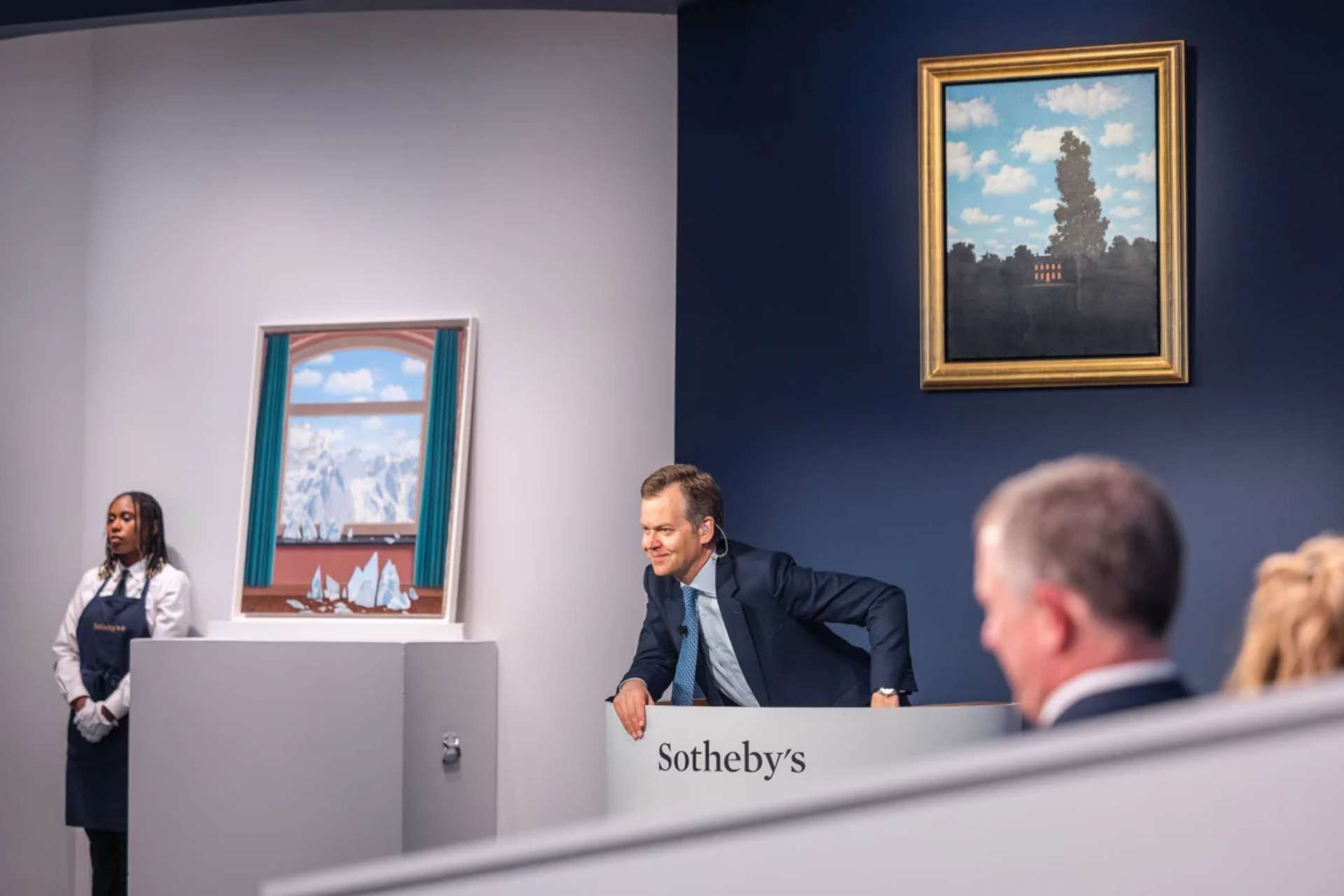 A photograph capturing a moment from Sotheby’s live auction, The Mo ostin Collection. The auctioneer leans over the podium, resting on one arm, eagerly awaiting the next bid. 