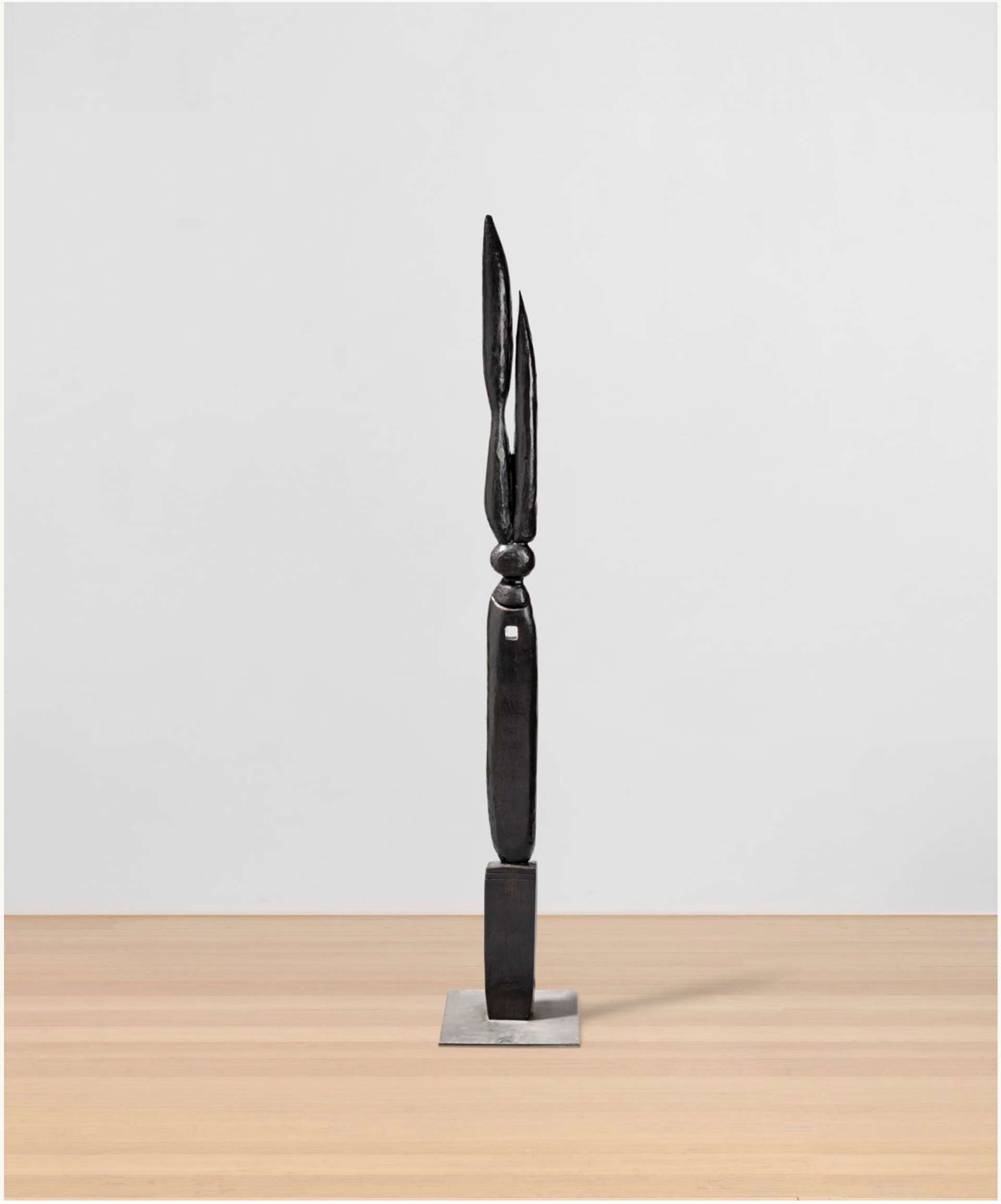 A black sculpture resembling a tall, skinny candle with three distinct parts. At the base, a sturdy foundation; in the middle, a slender column; and at the top, a flame-like structure. The sculpture evokes the image of a burning black candle.
