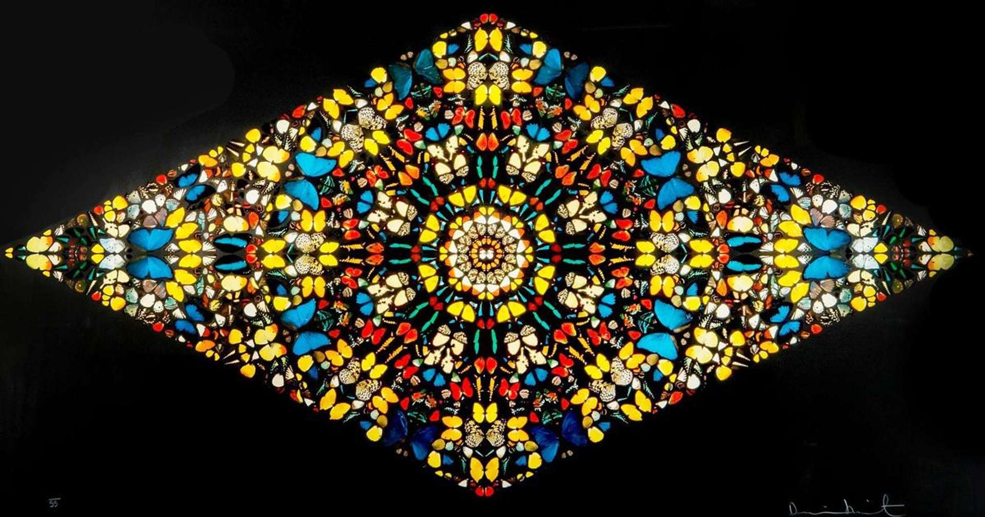 An image of the artwork Faithless by Damien Hirst. It consists of hundreds of colourful butterfly wings, arranged geometrically to create a mandala. The work is lozenge-shaped against a black background.