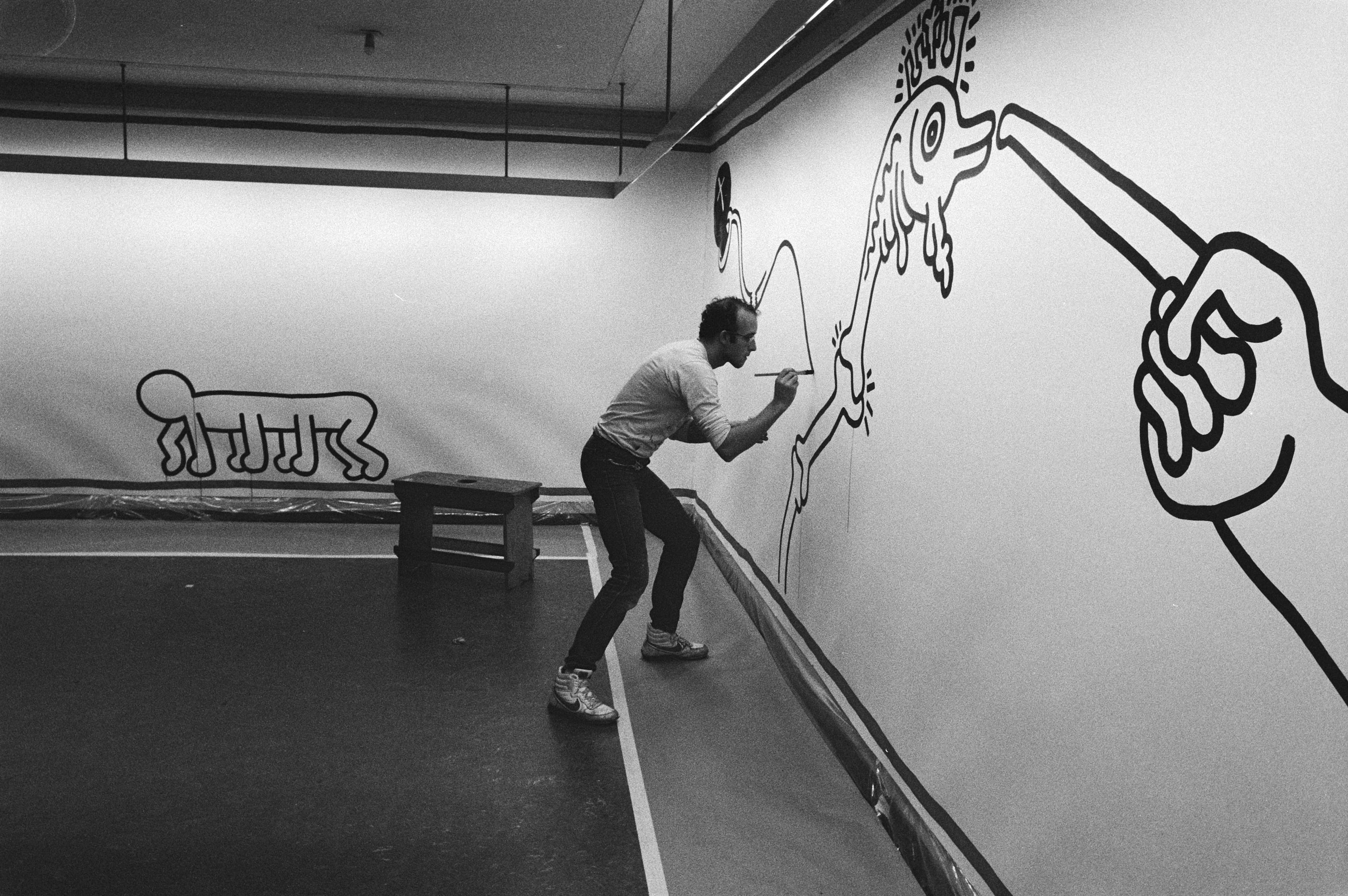 Keith Haring painting a cartoon fish onto a wall in his distinctive linear style