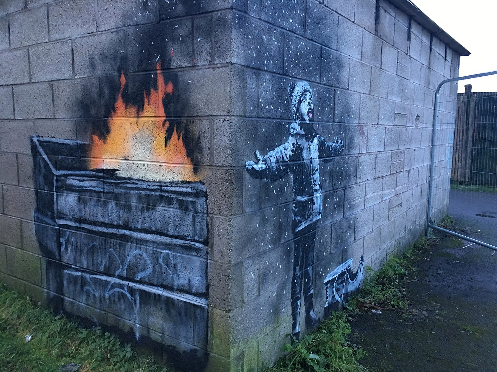 This work by Banksy is done at the corner of a building; one side shows a burning dumpster, while the other shows a happy young boy playing in the resulting ashes.