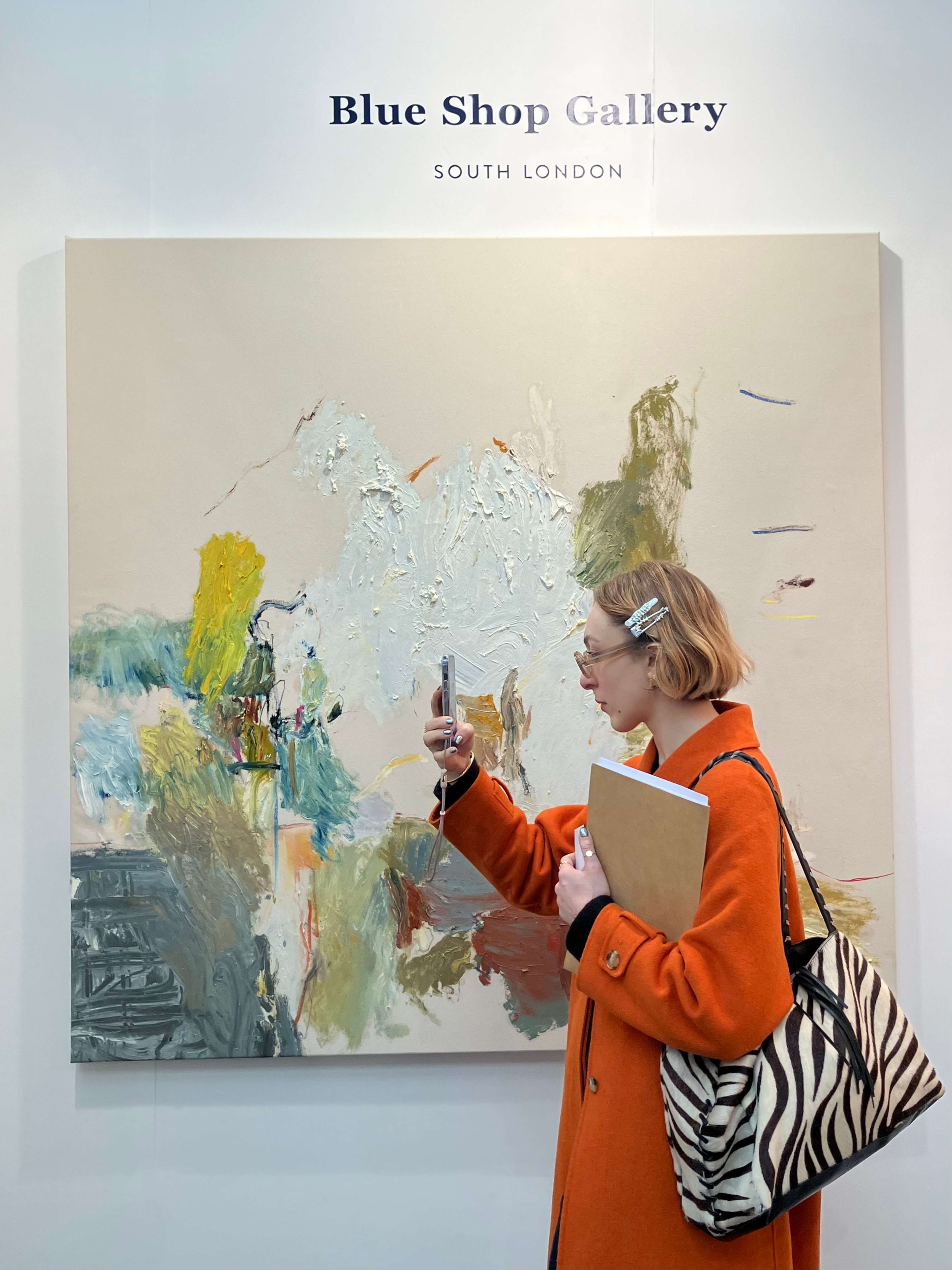 A young woman standing in front of a large piece of art takes a photo of something out of the frame.