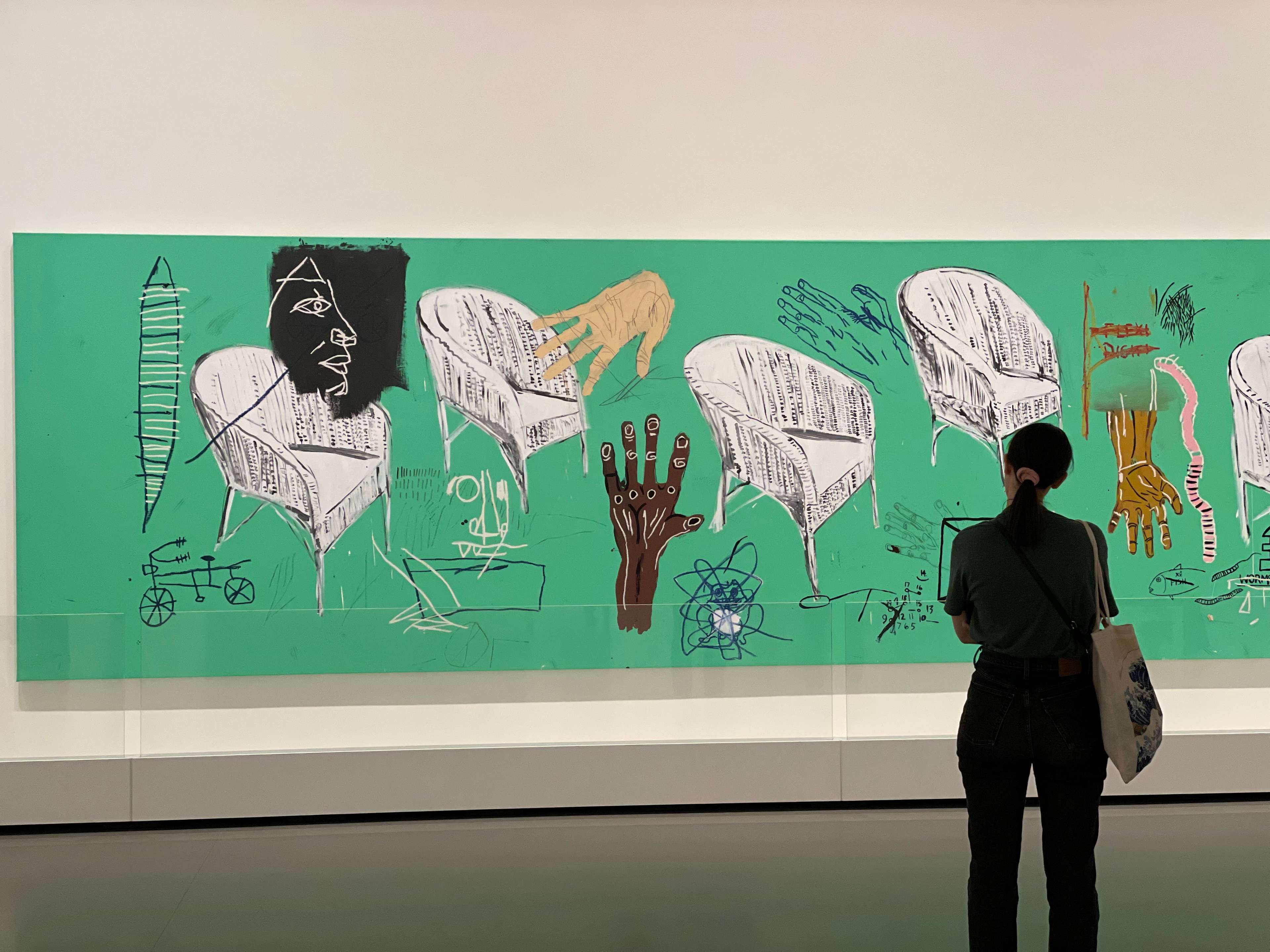 A green canvas with white chairs and abstract neo-expressionist figures