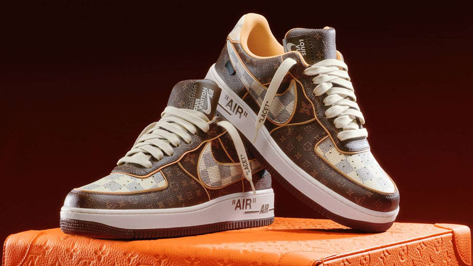 A pair of trainers covered with the Louis Vuitton monogram rested on top of an orange Louis Vuitton trunk