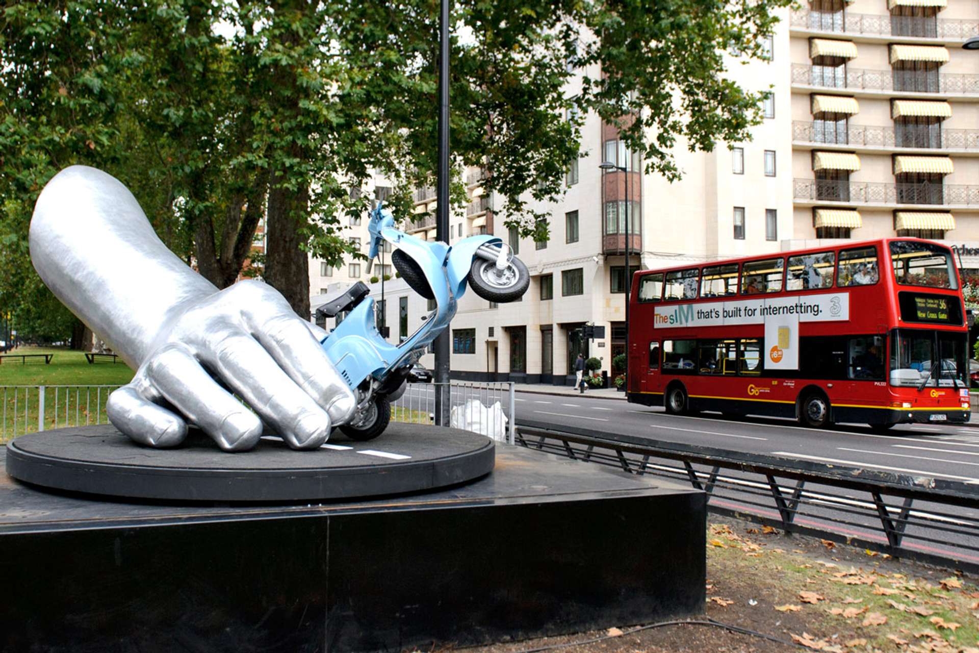 A bronze sculpture titled "Dolce Vita" featuring a large hand emerging from the ground, holding a vintage scooter, created by artist Lorenzo Quinn in 2013.