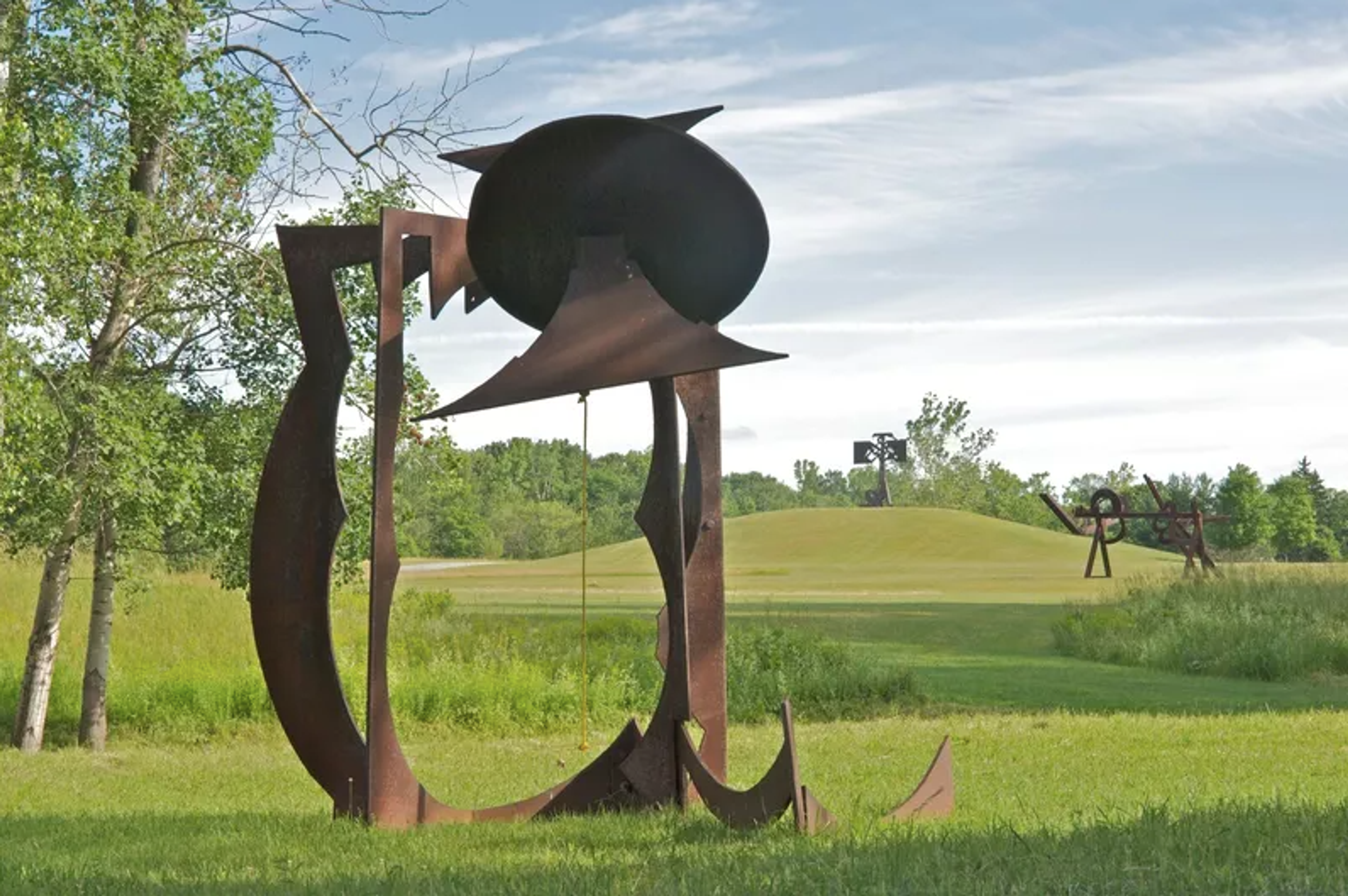 An outdoor steel sculpture titled "For Chris" created by Mark di Suvero in 1991. The sculpture features several large, curved steel beams painted in a bright shade of red that intersect and crisscross each other to create a dynamic structure.