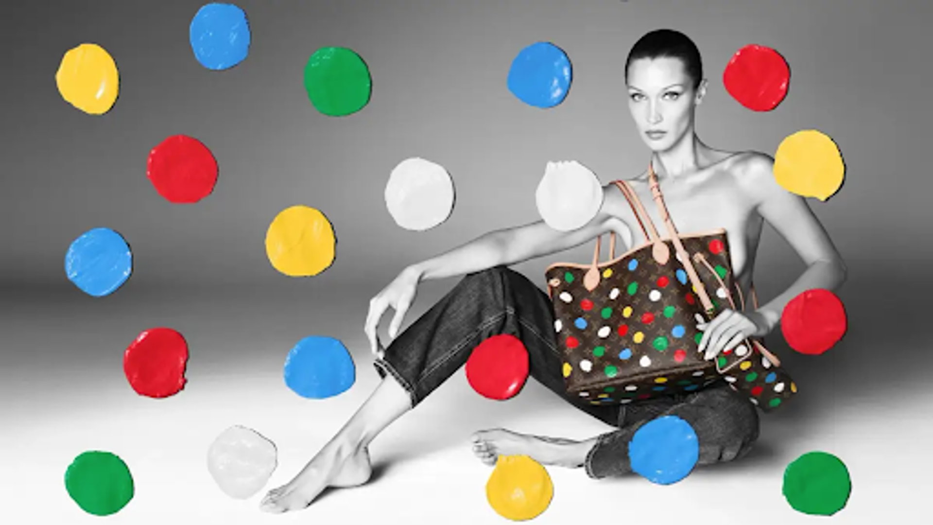 Greyscale photograph of a woman modelling a Louis Vuitton handbag with colourful Kusama polka dots
