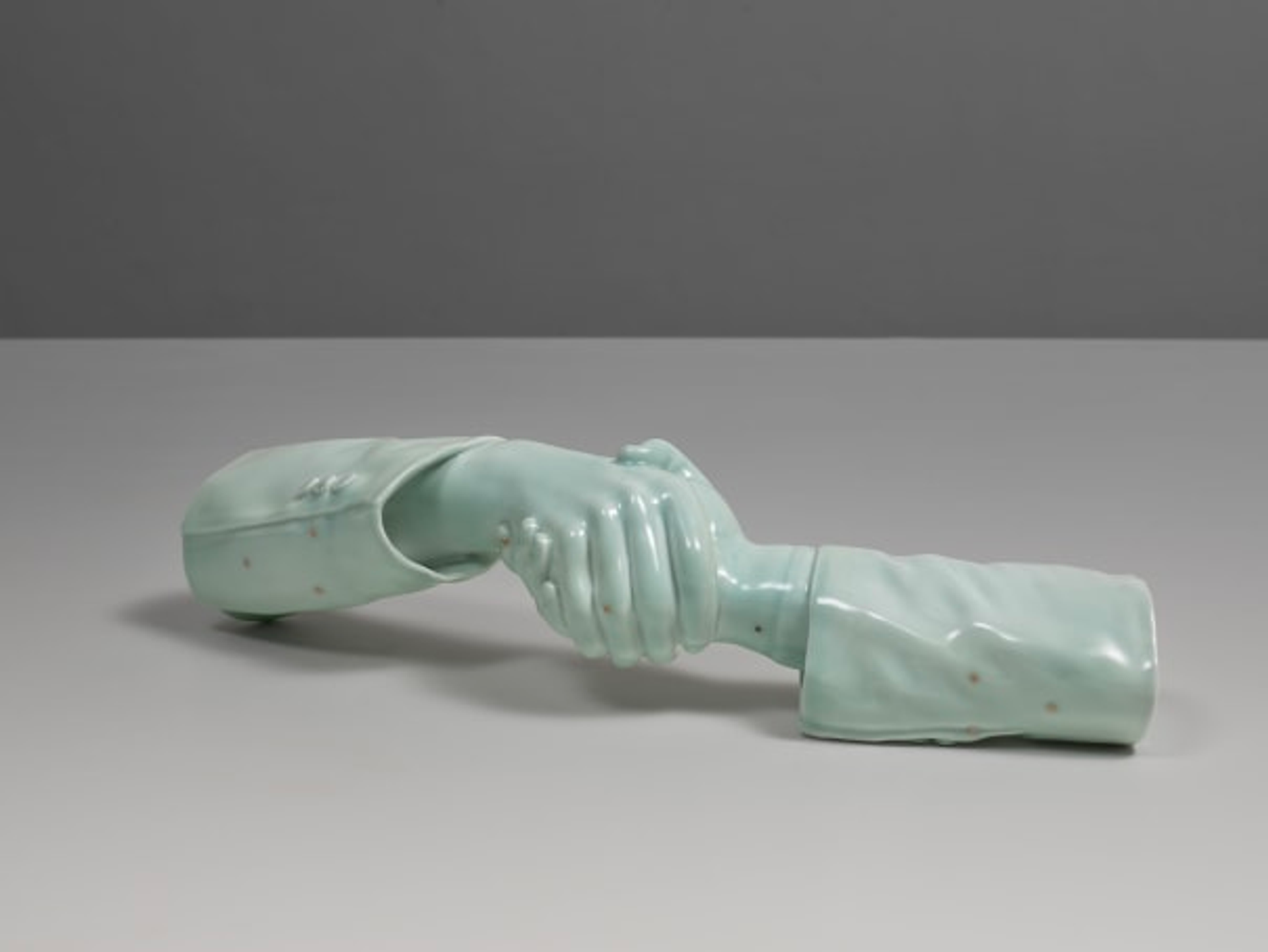 A green porcelain sculpture of two hands shaking