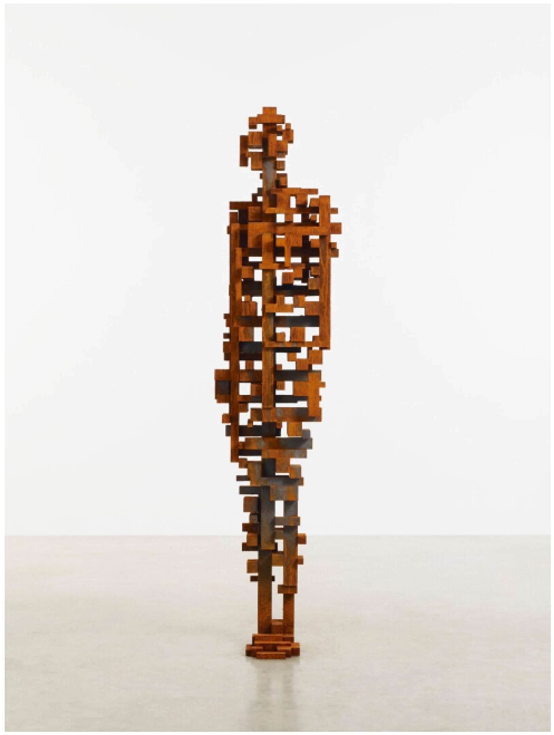 A life-sized sculpture of a human figure, constructed from interlocking steel beams carefully positioned to create voids, showcasing the balance and precision of the artwork. The sculpture captures the essence of the human form, standing upright with feet together and arms at the sides, devoid of specific features. The photograph captures the sculpture in an empty white gallery space.