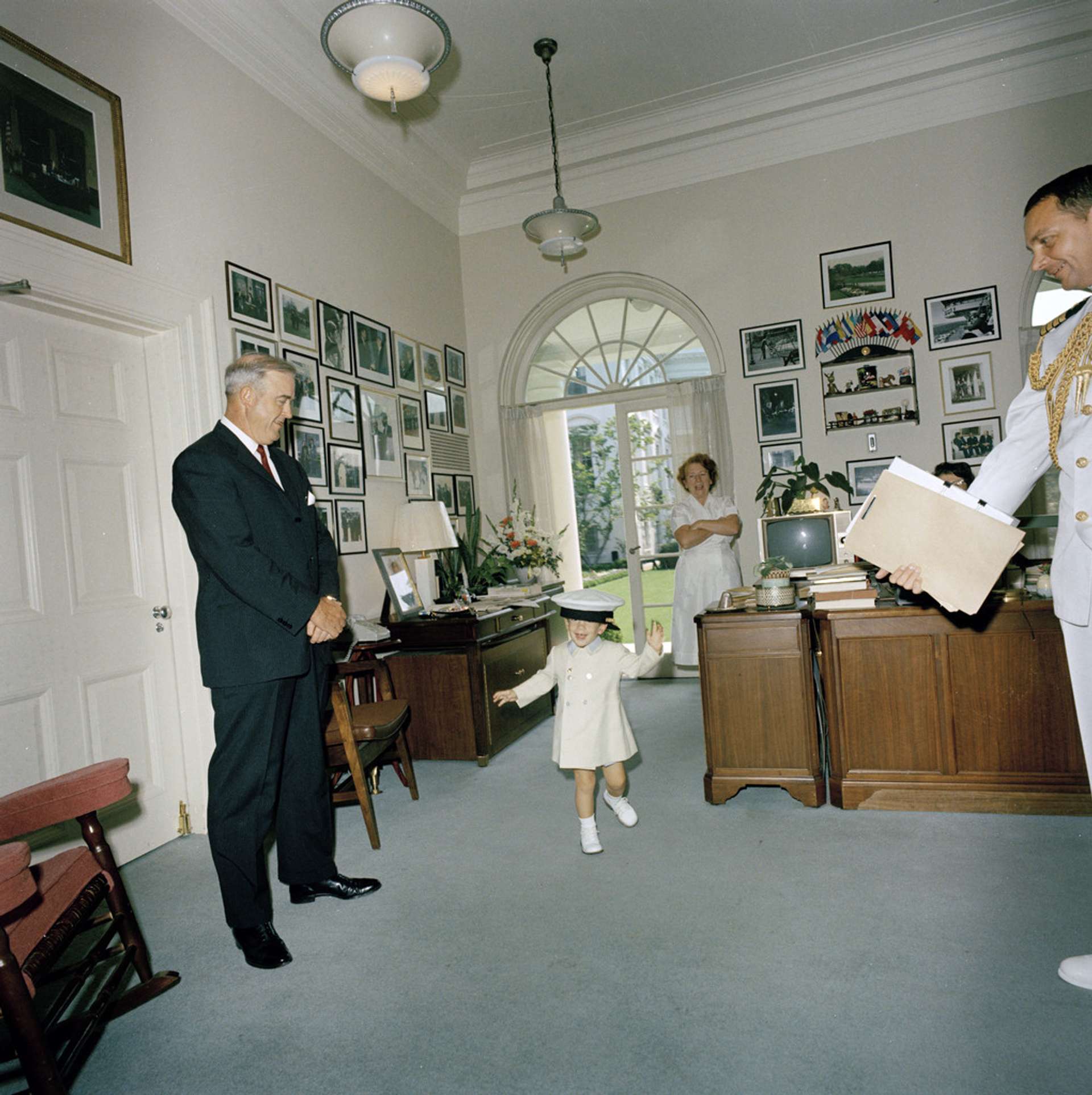 A photograph of a young boy running round in the White House playing with a hat. 