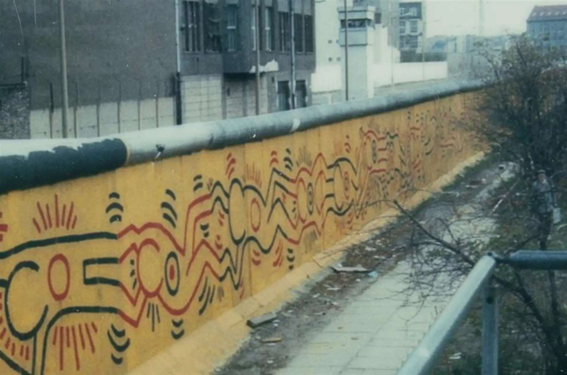 Keith Haring's mural on the Berlin Wall, depicting a chain of conjoined figures in red and black against a yellow background.