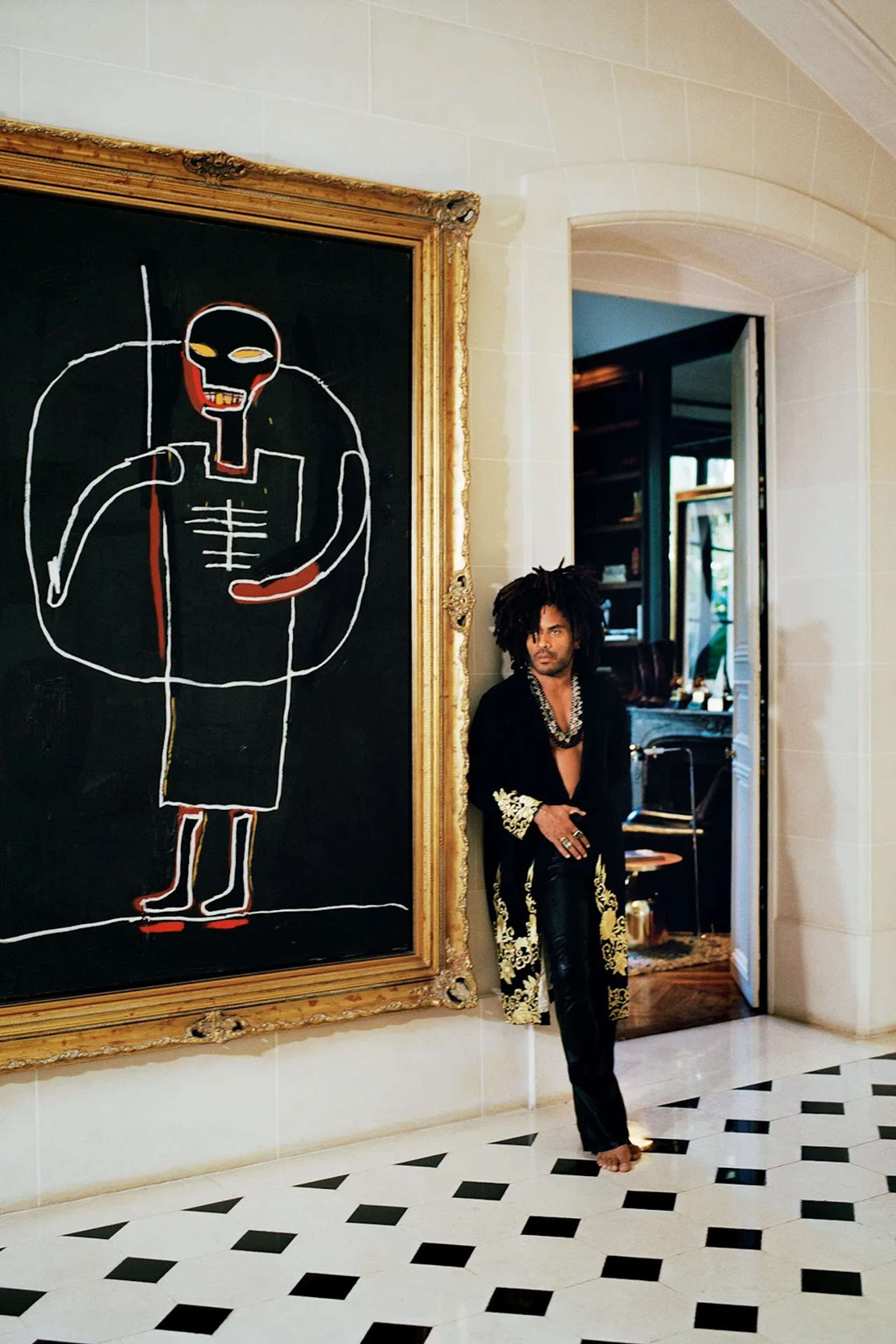 Photograph of Lenny Kravitz standing next to a Jean-Michele Basquiat painting in his home. Photograph of Lenny Kravitz standing next to a Jean-Michele Basquiat painting in his home. 
