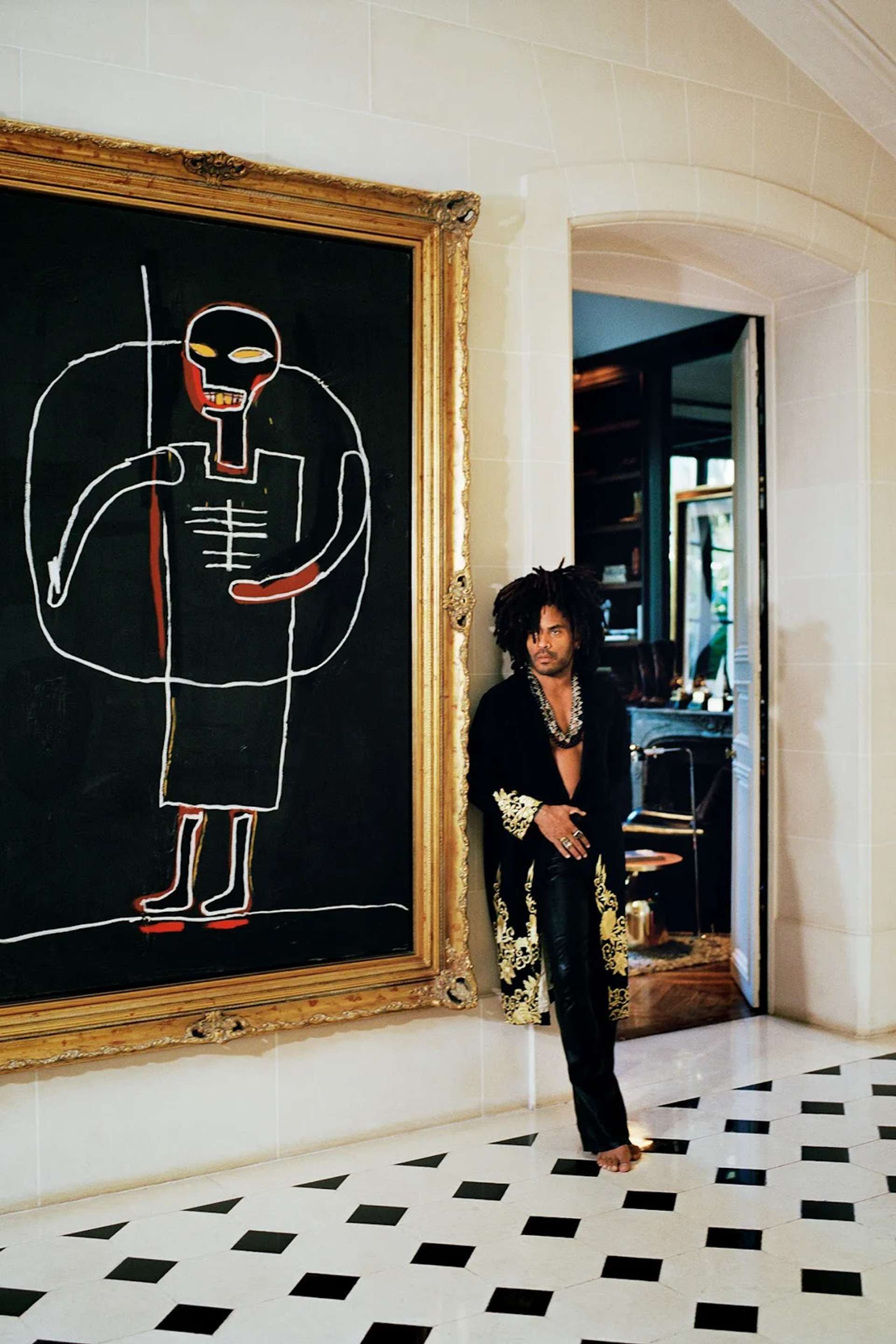 Photograph of Lenny Kravitz standing next to a Jean-Michele Basquiat painting in his home. Photograph of Lenny Kravitz standing next to a Jean-Michele Basquiat painting in his home. 