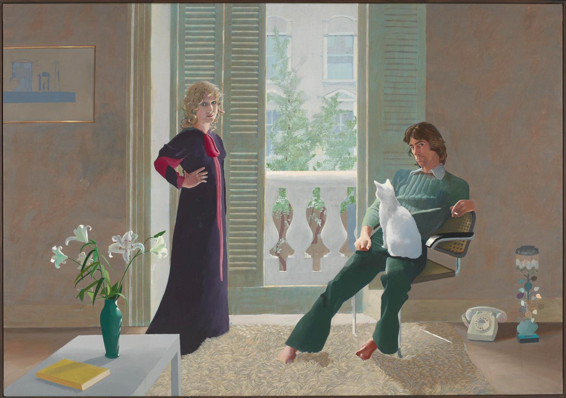 A couple pose in their London apartment. A man in green sits in a chair with a cat on his lap; a woman stands next to him with her hands on her hips. Both stare directly at the viewer.