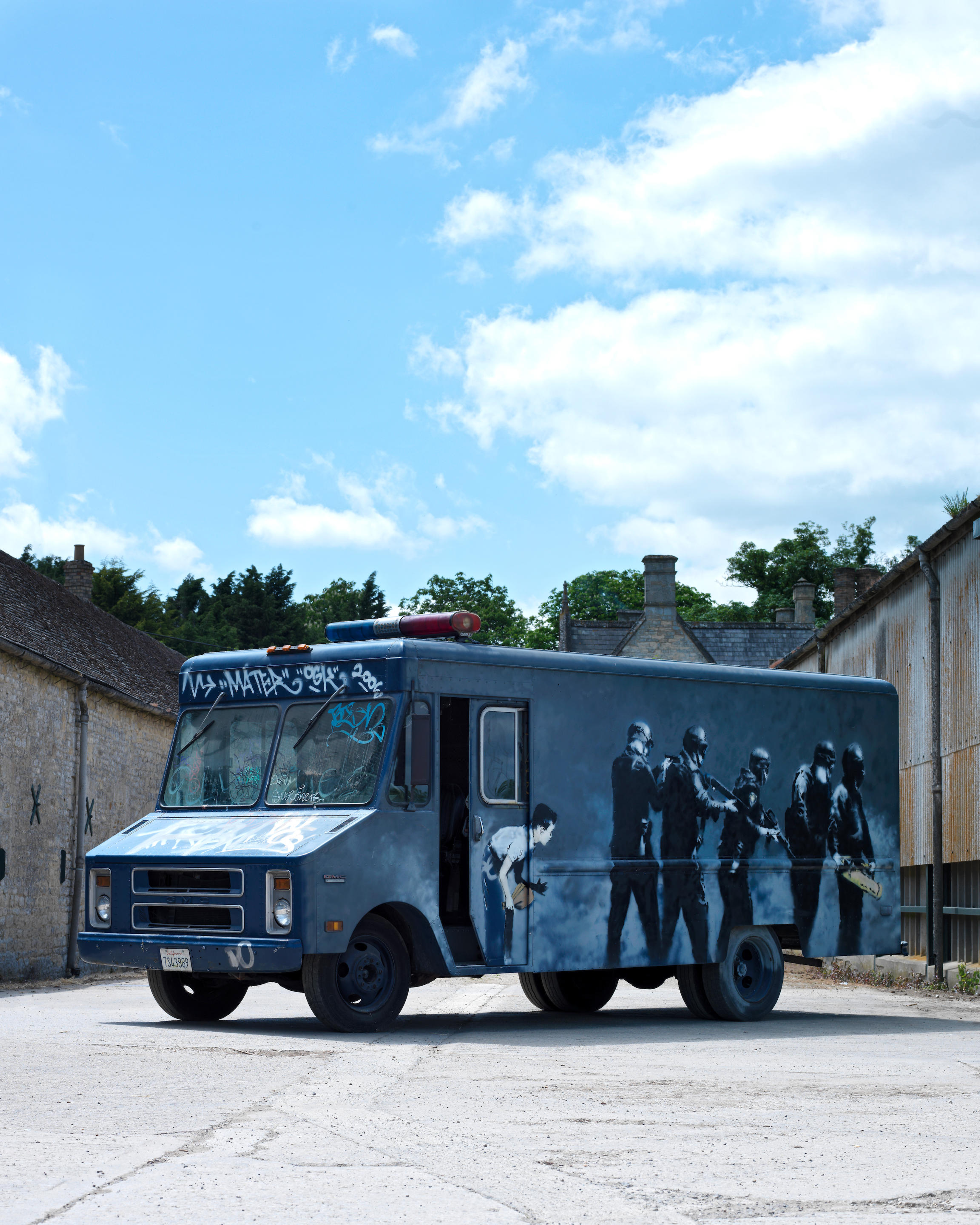 This photograph shows Banksy's SWAT Van, an actual van that has been painted with a mural depicting a group of SWAT officers, with a young boy looking at them.