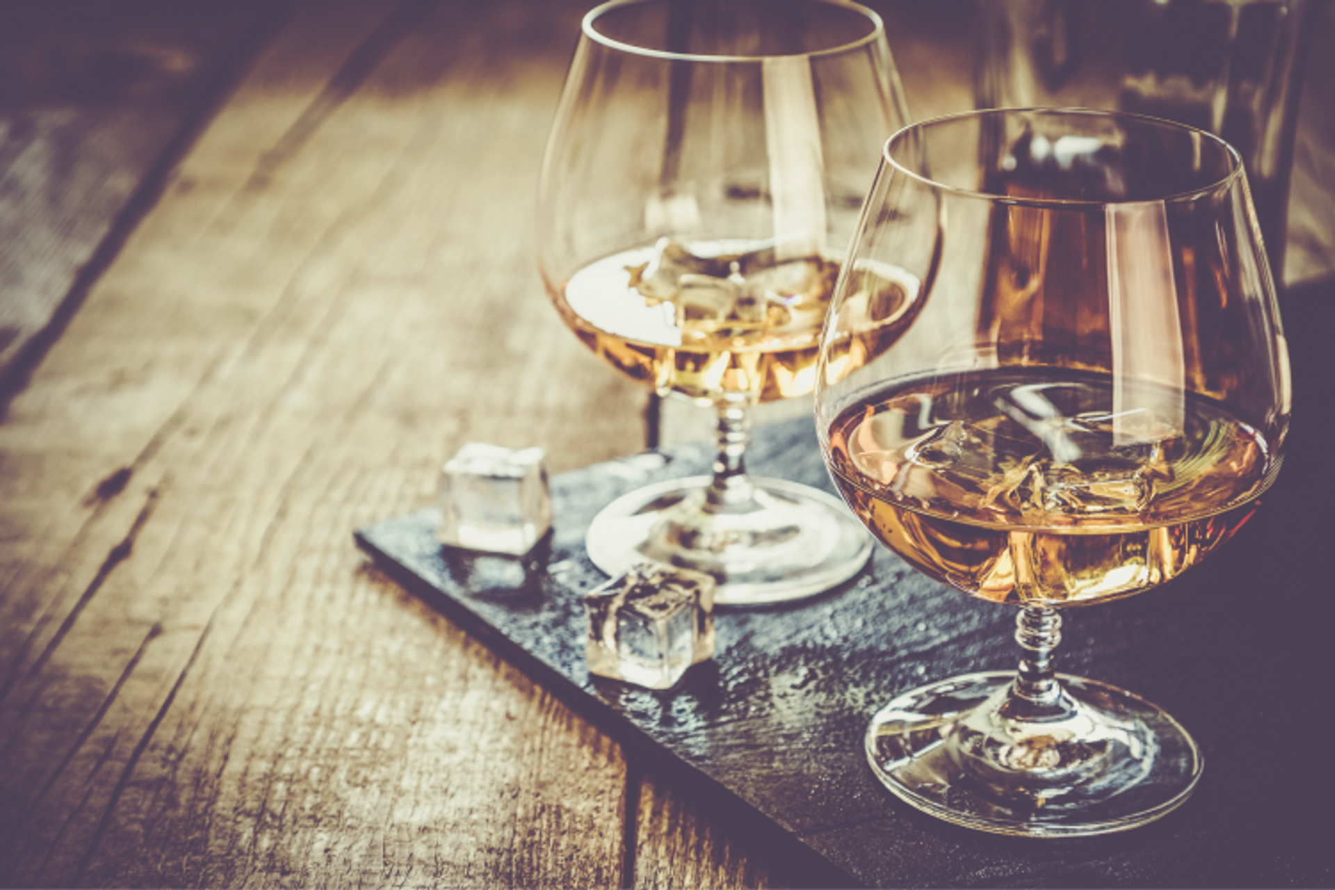 An image of two glasses of whisky on ice, on a wooden table.