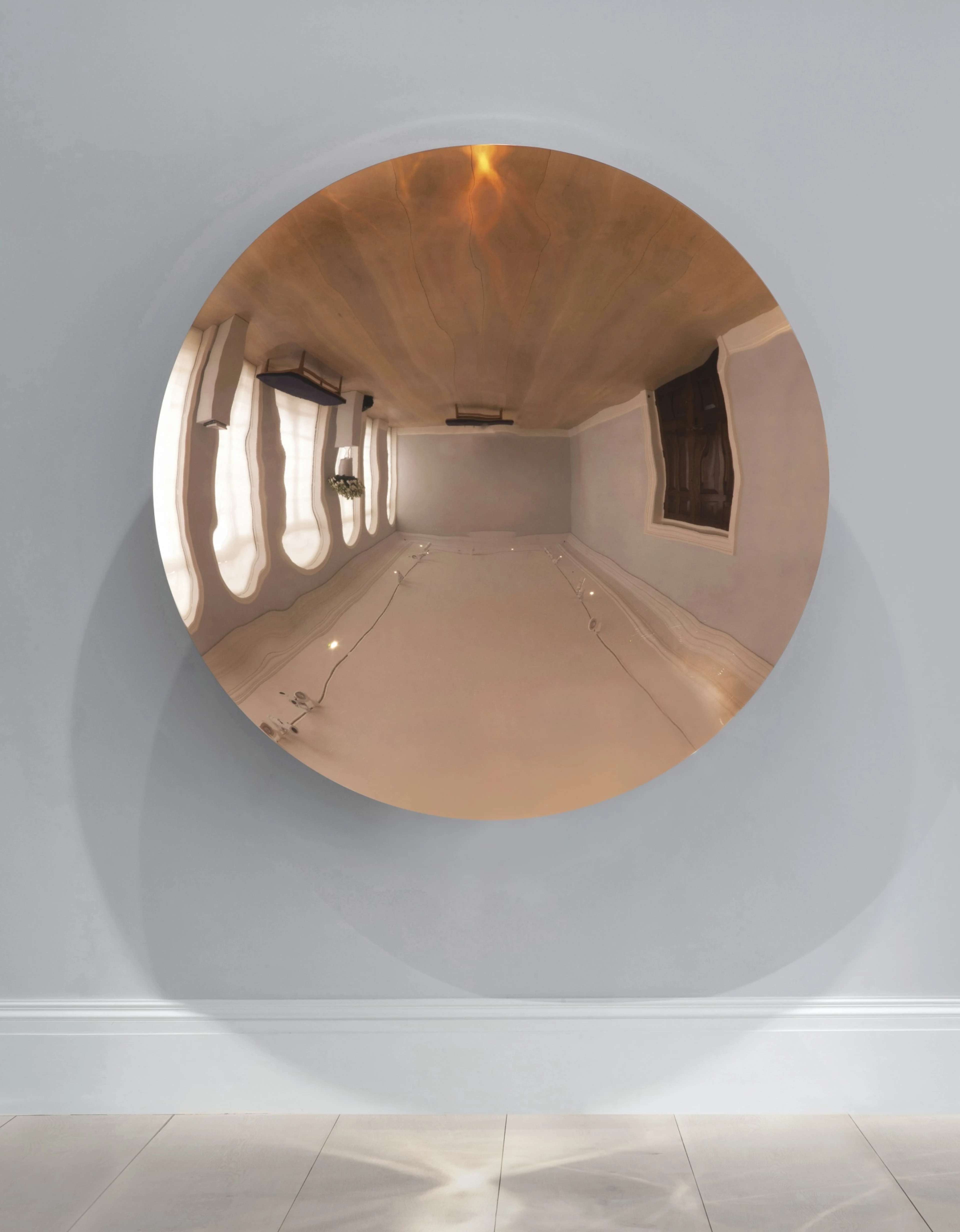 A concave copper mirror disc reflecting and distorting an interior gallery space, creating an illusory depth effect.