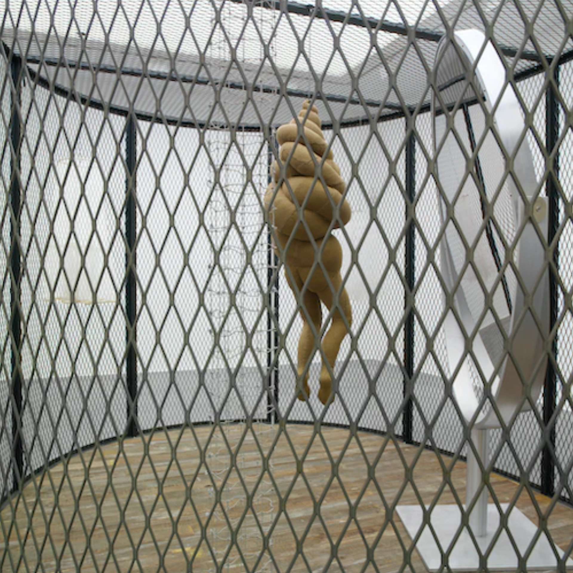 A fabric sculpture of a woman wrapped  up with fabric inside a cage with a mirror.
