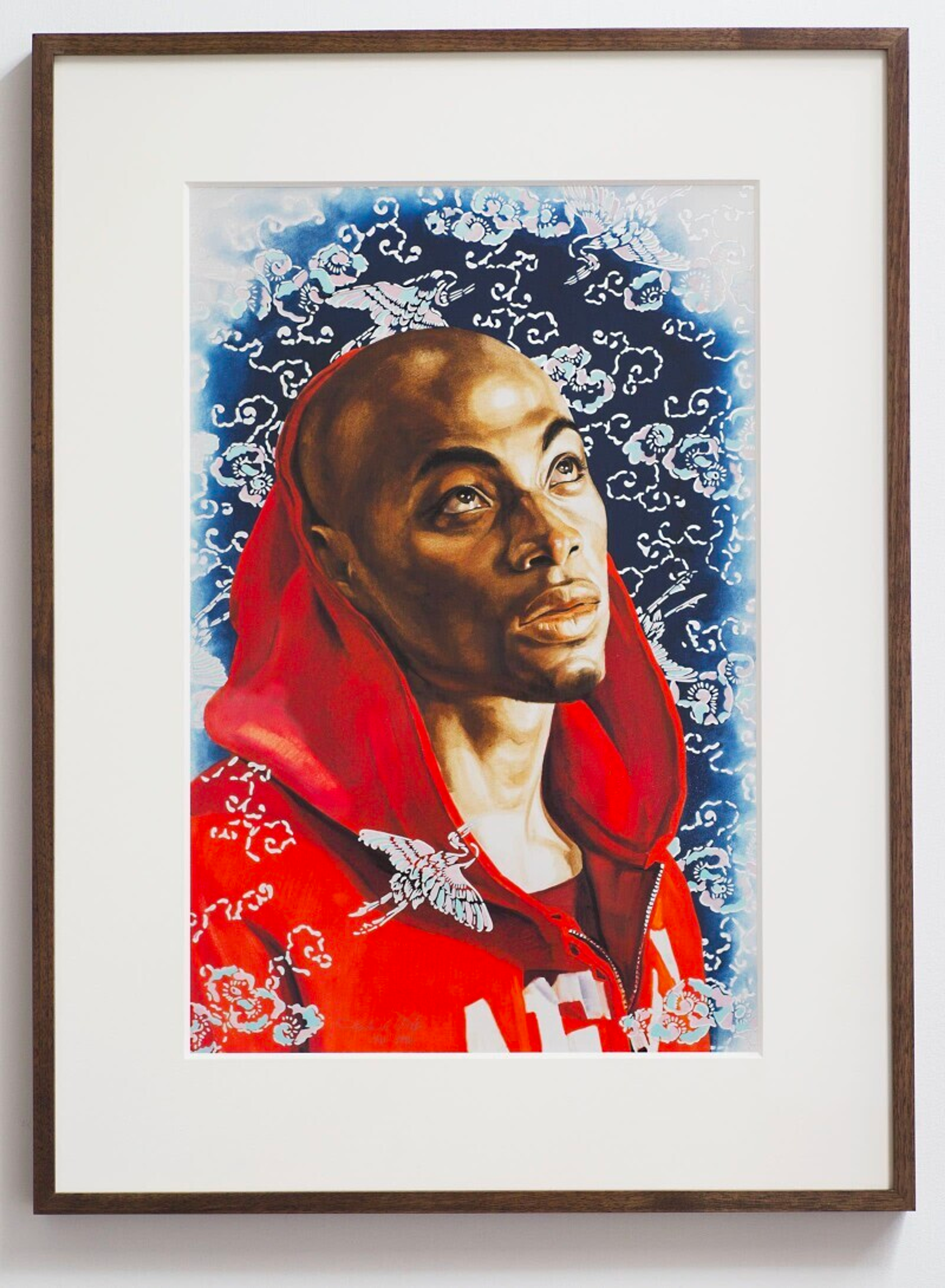 A printed portrait of a young black man in a vibrant red hooded sweatshirt, looking up with his side profile. Blue foliage backdrop adds depth.