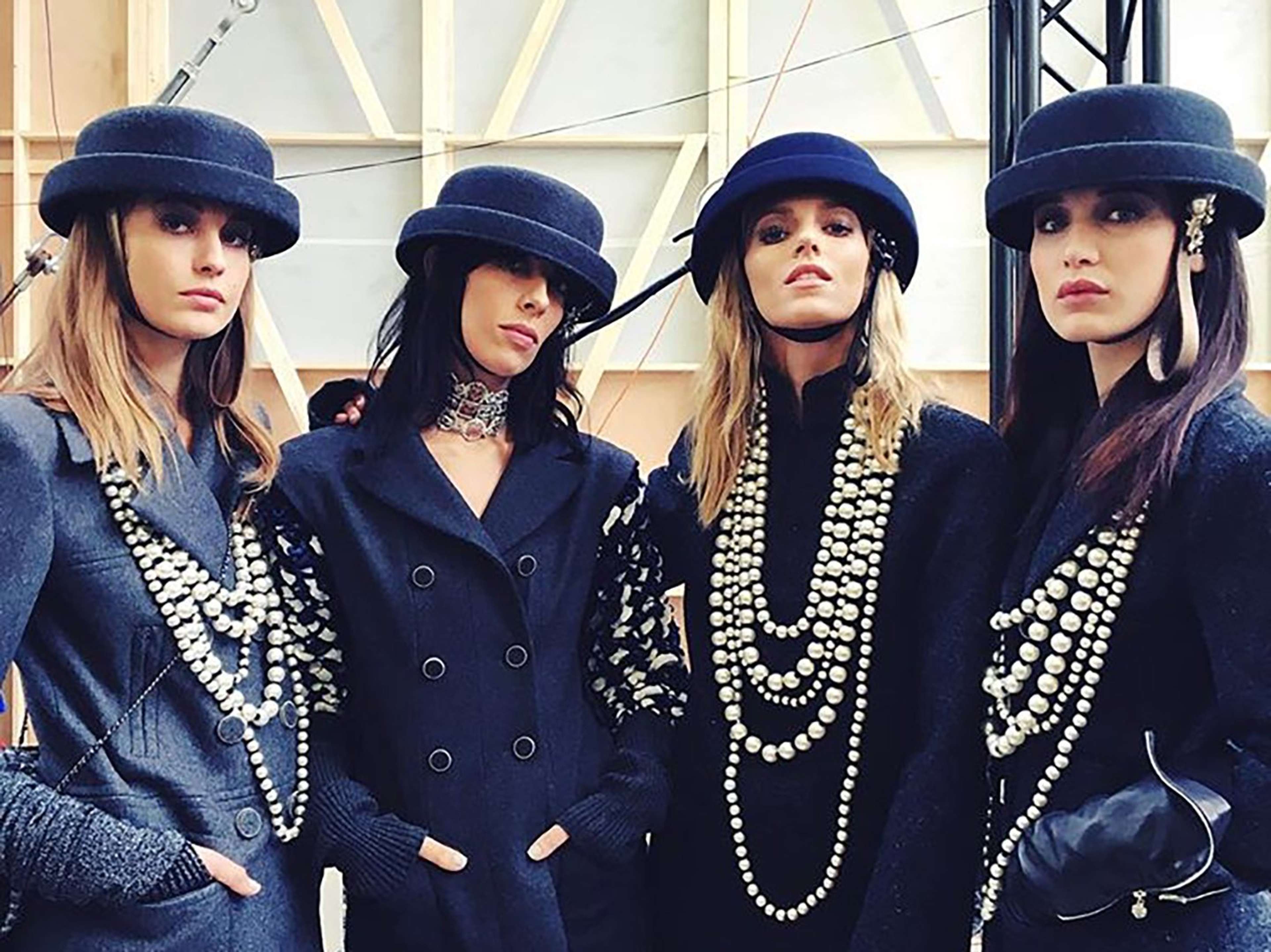 An image of four models, all dressed in black, clad in many pieces of Chanel costume jewellery.