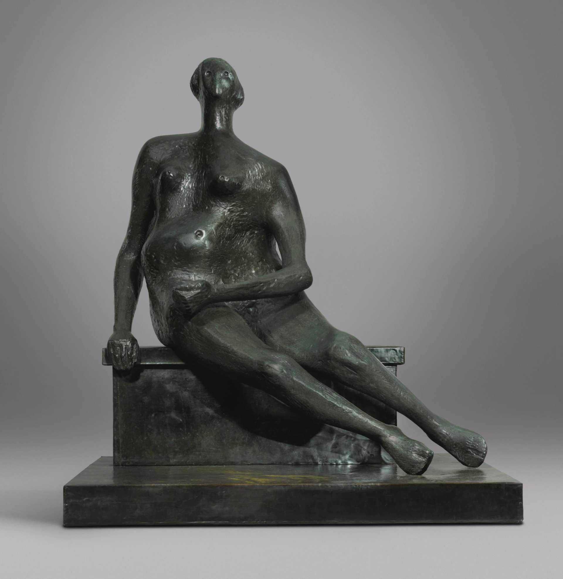 A bronze sculpture by Henry Moore depicting a seated woman with a broad torso and a prominent pregnancy. The sculpture is positioned on a pedestal.