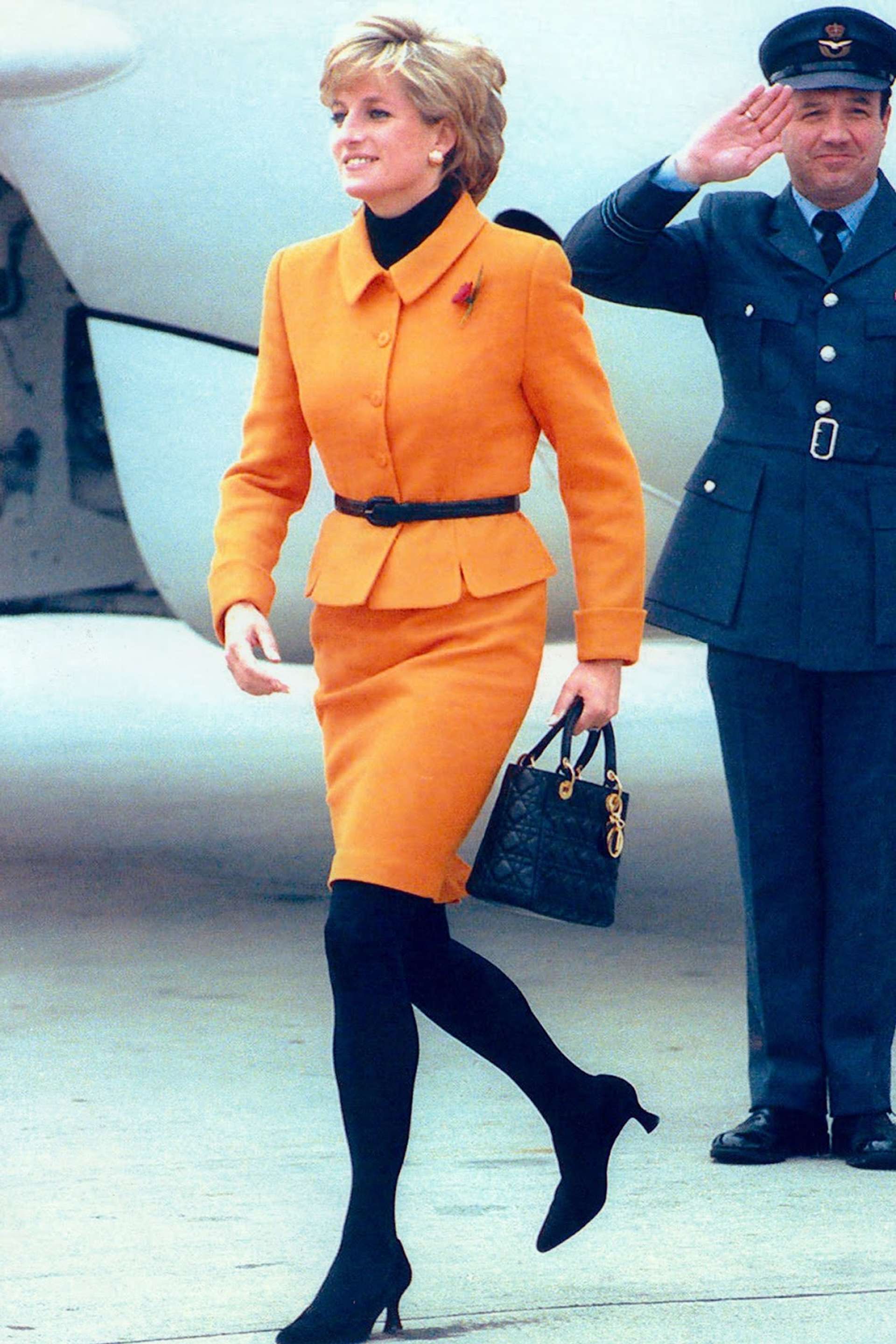 An image of Diana, Princess of Wales, dressed in orange, carrying her black Lady Dior handbag in 1996.