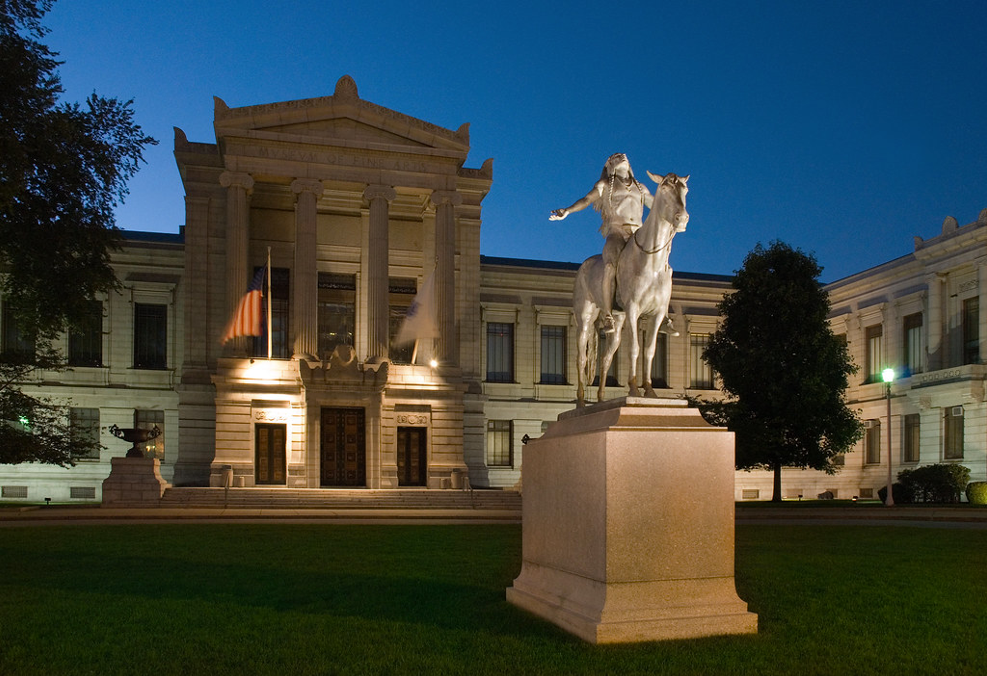 An outdoor image of the Museum of Fine Arts, Boston in the evening. It shows the building's facade and an equestrian statue.