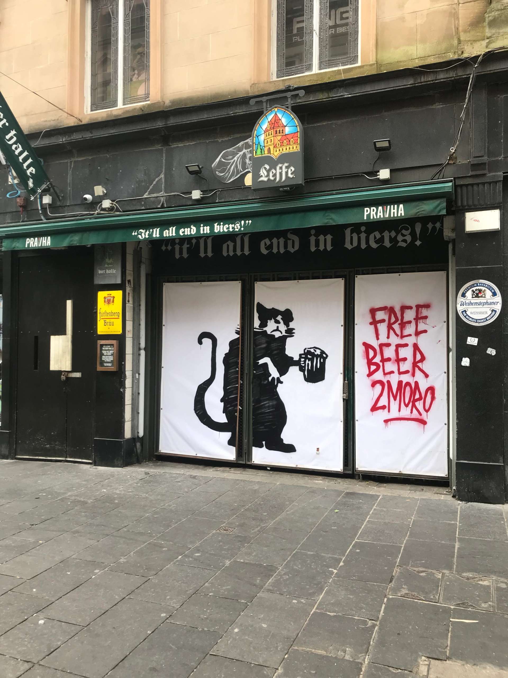 A graffiti artwork of a rat holding a pint of beer with the words: “FREE BEER 2MORO” sprayed in red next to it on the facade of a pub