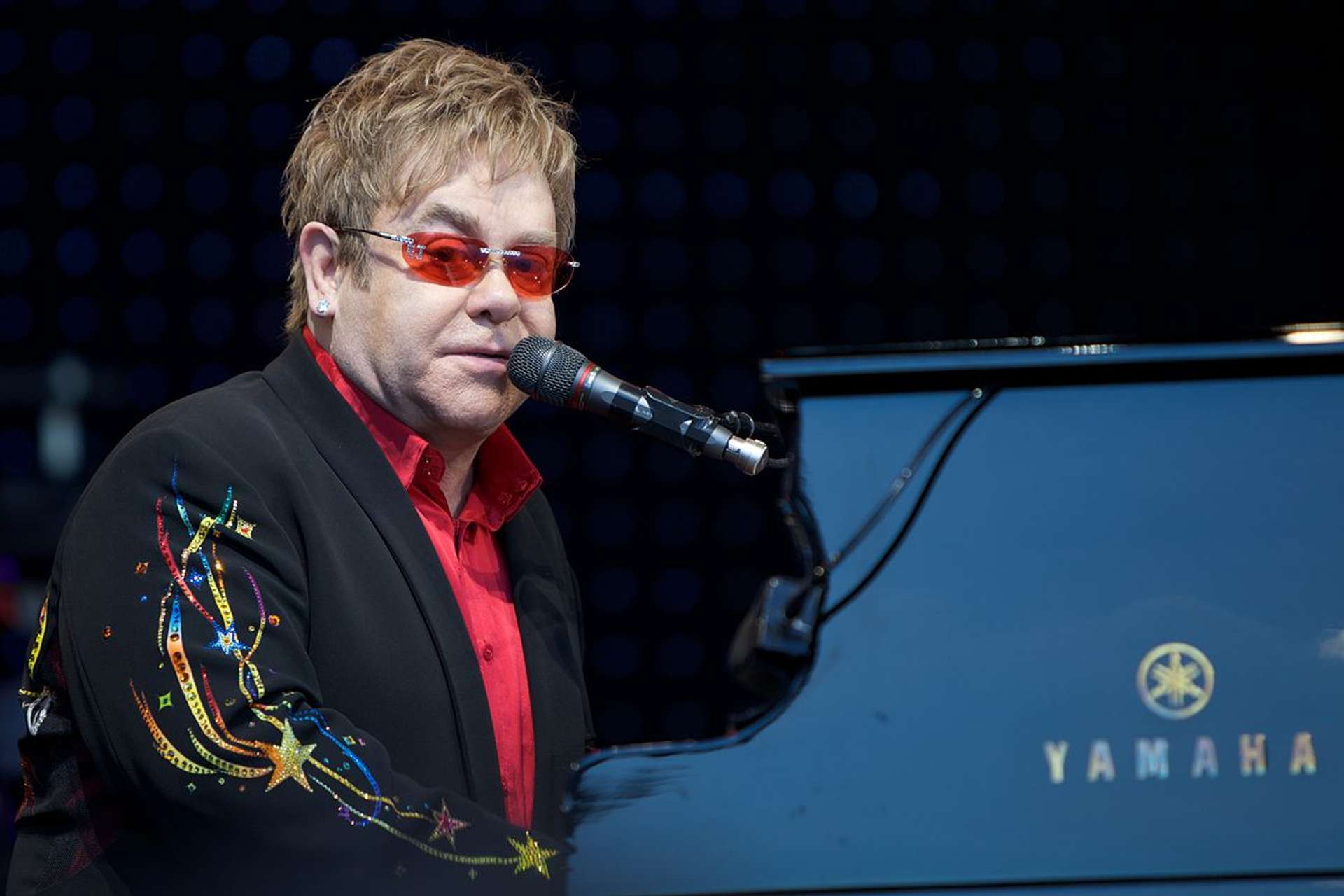 Sir Elton John performing in Norway, seated at a piano with a microphone.